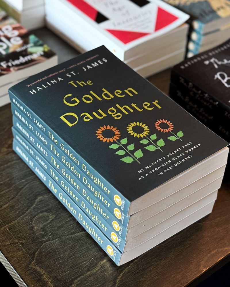 A stack of the book THE GOLDEN DAUGHTER by Halina St. James. The cover features three illustrated sunflowers.
