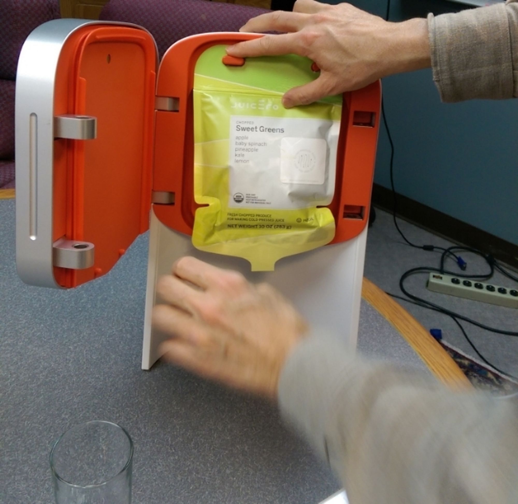 A Juicero device white and red plastic with a green fruit bag.