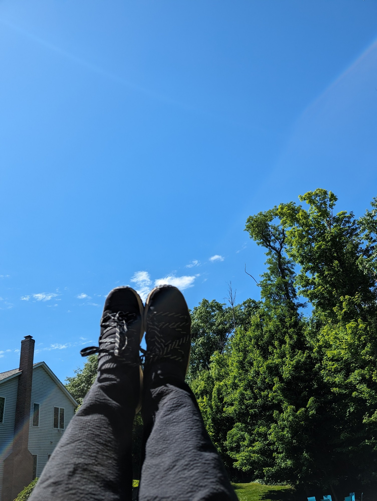 Legs shorn in black pants, pointed toes. The background is the blue sky, trees, and a large house .