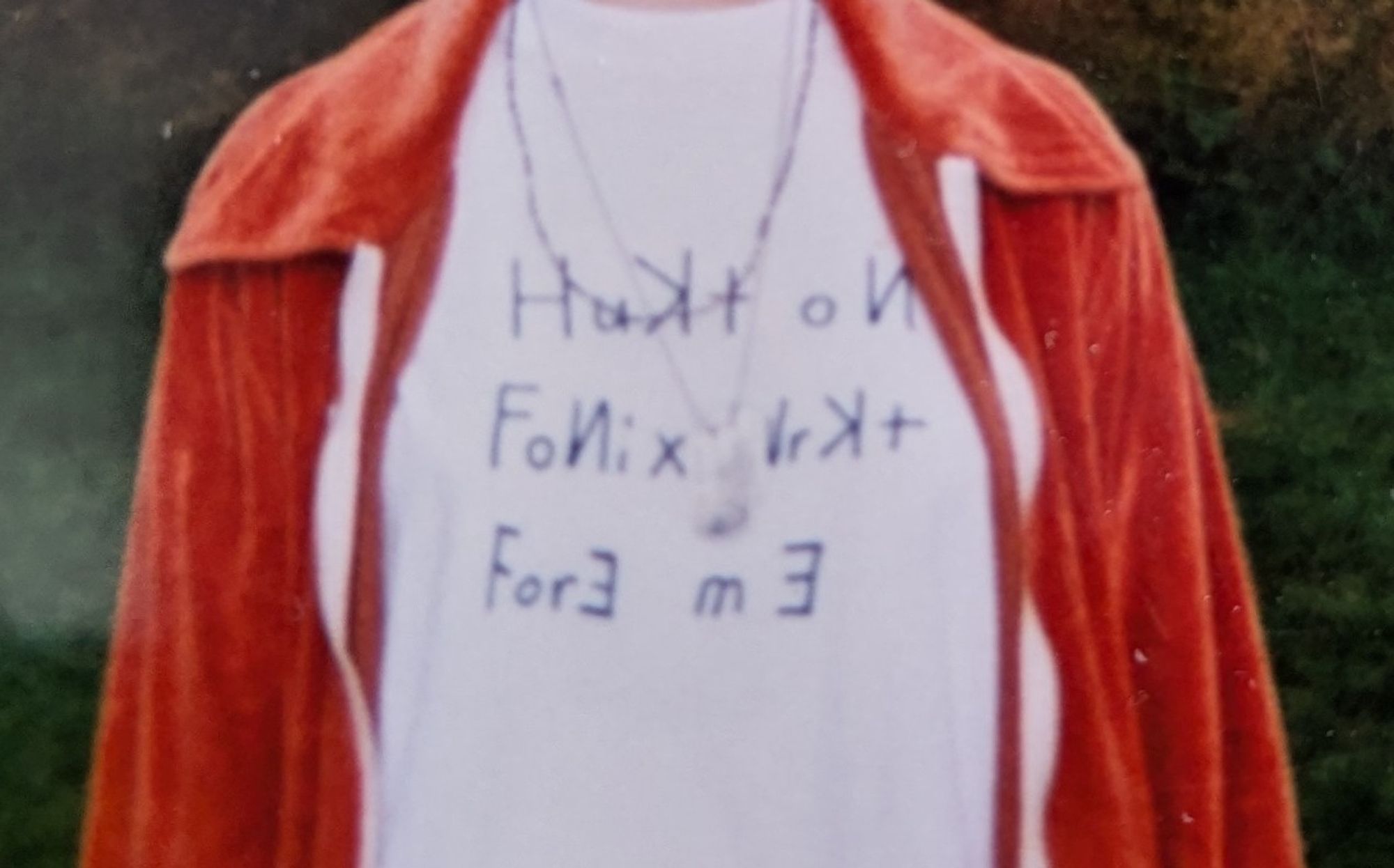 Cropped photo of a Hukt on fonix wrkt fore me t-shirt under an orange velour jacket.