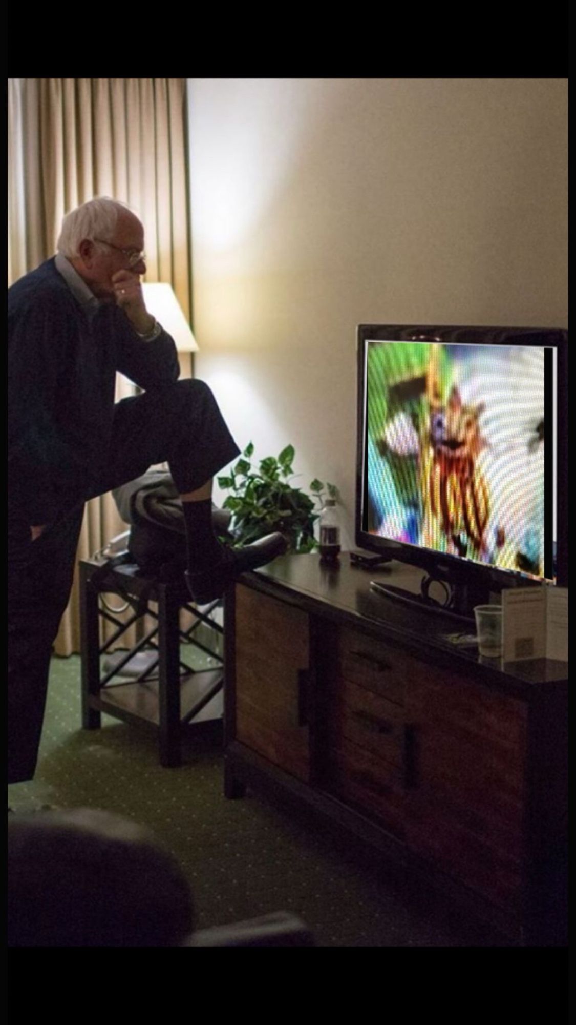 Bernie Sanders looking at a tv. The tv has a messed up looking sun from fnaf on the screen.