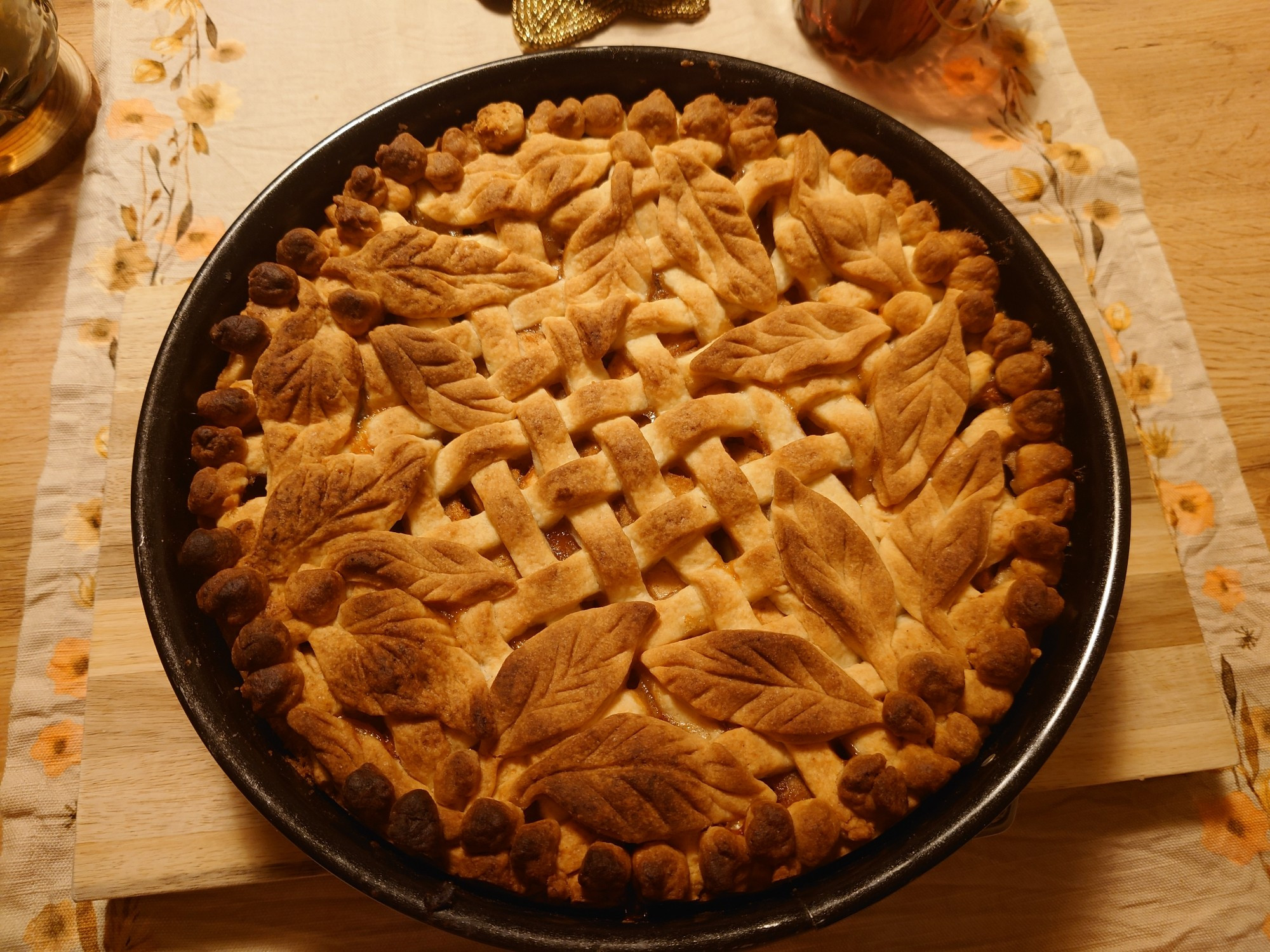 The apple pie in a close up picture. The basket patterned and leaf decorated crust has a warm brown tint. Baked to perfection. A picture you can almost smell.