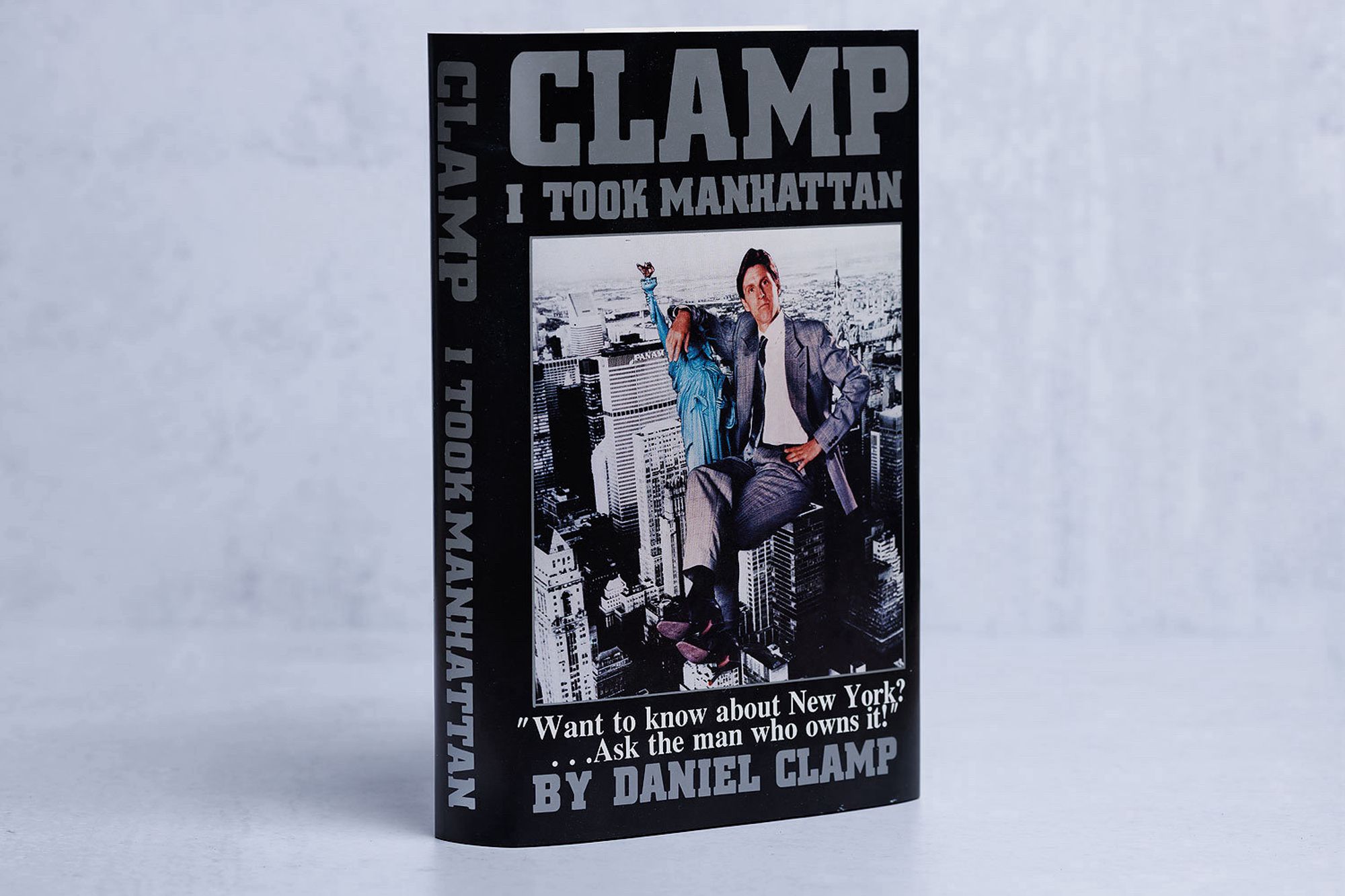 Fake book called “Clamp: I Took Manhattan.” Subtitle: “Want to know about New York? Ask the man who owns it.” Cover is a photo of an insufferable douchebag sitting on top of the Manhattan skyline.