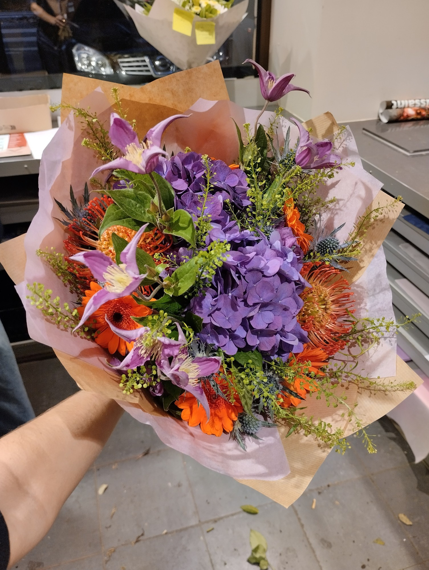 Bouquet de fleurs hortensia violets, germinis oranges, chardons bleuté, Thlaspi (feuillage vert) et clématites violettes 