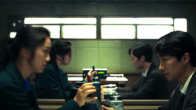 Decision to leave (2022). a man and a woman sit across from each other in an interrogation room. 