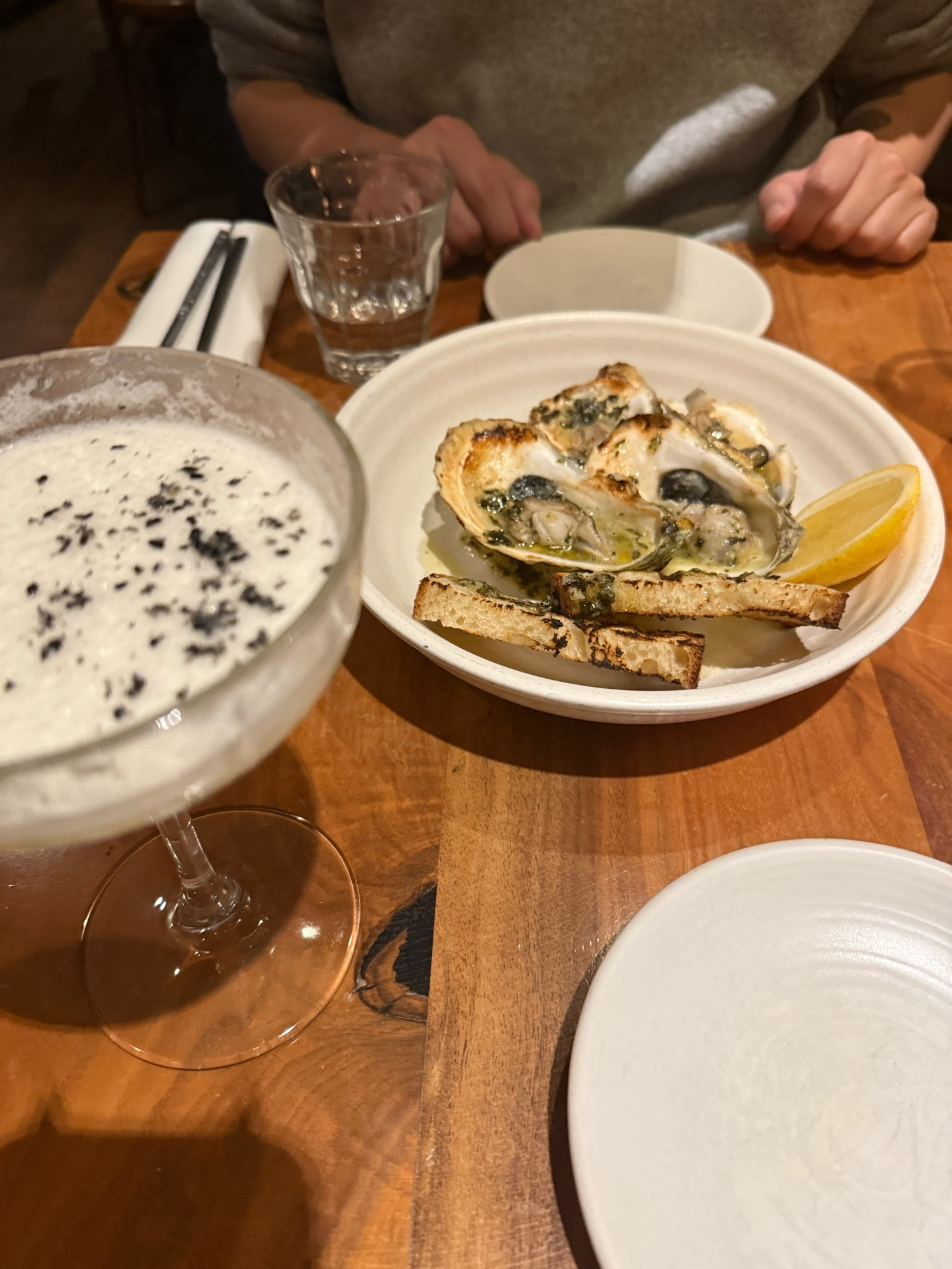 table with an egg white lemongrass soju sesame oil cocktail and a plate of grilled oysters and bread 