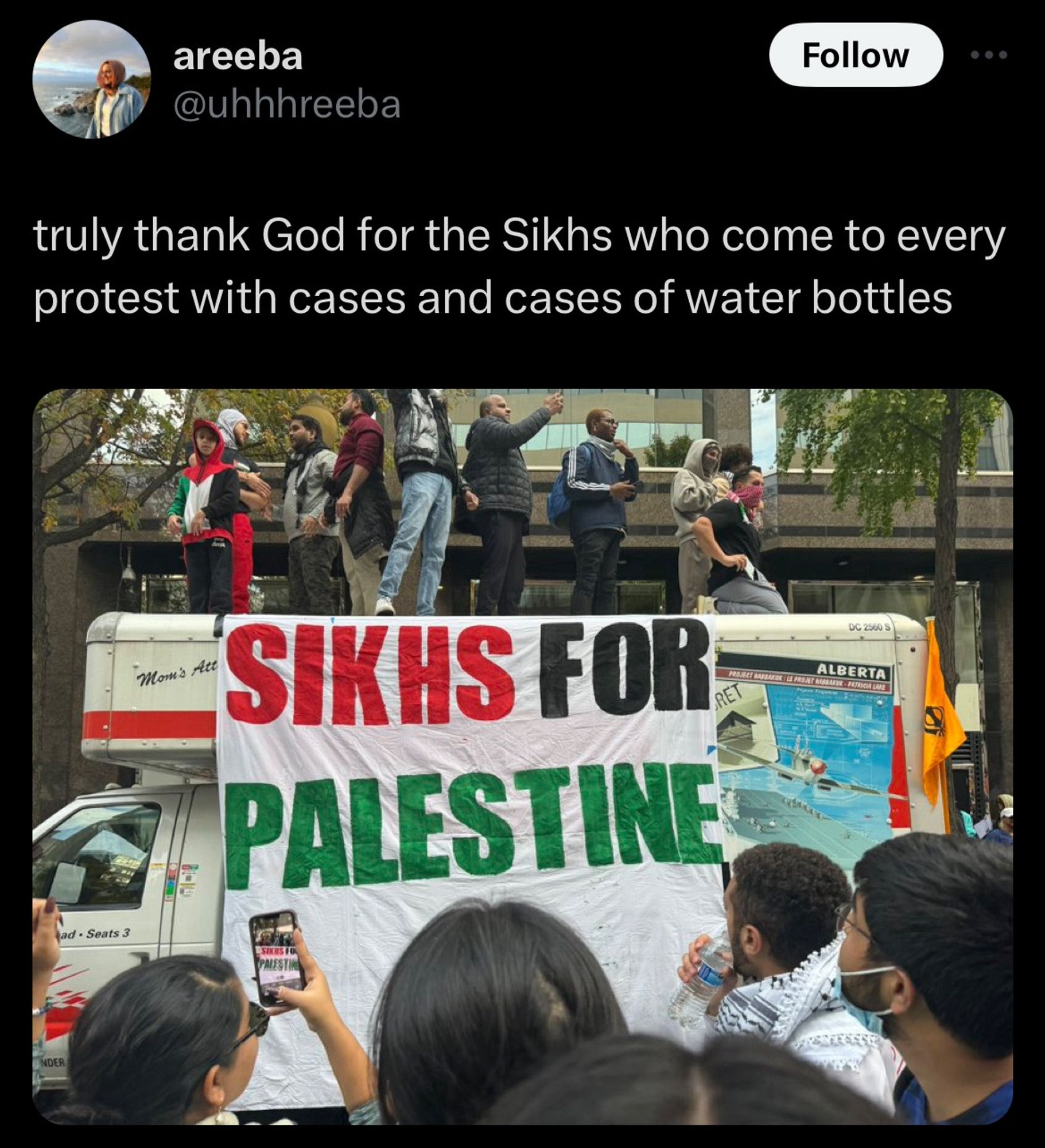 tweet from @uhhhreeba “truly thank God for the Sikhs who come to every protest with cases and cases of water bottles” attached is an image of people standing on top of a white truck in a protest that has an enormous cloth sign on it that says SIKHS FOR PALESTINE