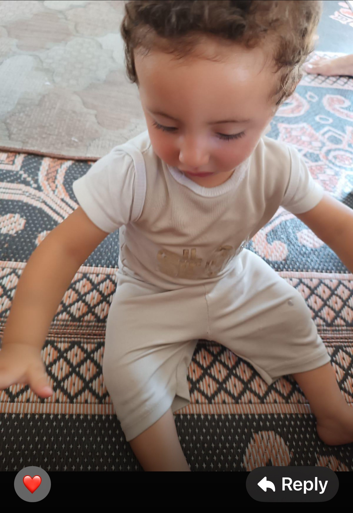 baby hamoud, a small boy with curly brown hair and large brown eyes, sitting on a rug in a tent 