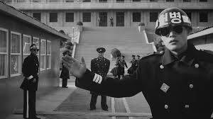 joint security area (2000). black and white grainy photo of a soldier interceding between someone taking a photo and the subject of the photo, another soldier at the DMZ 