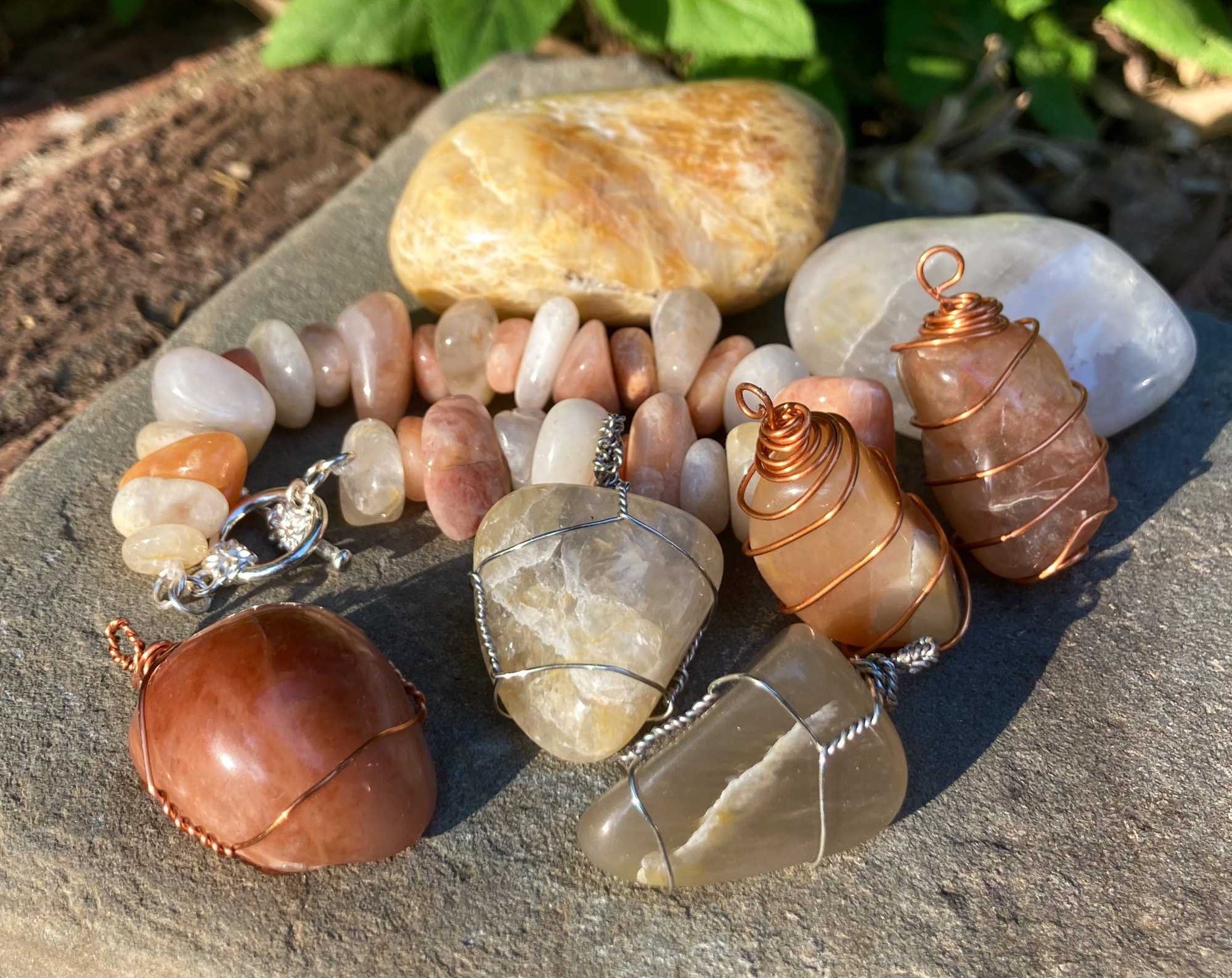 A collection of multicolored wire-wrapped tumbled quartzite stones arranged with a bracelet and two larger stones on a flat gray rock.