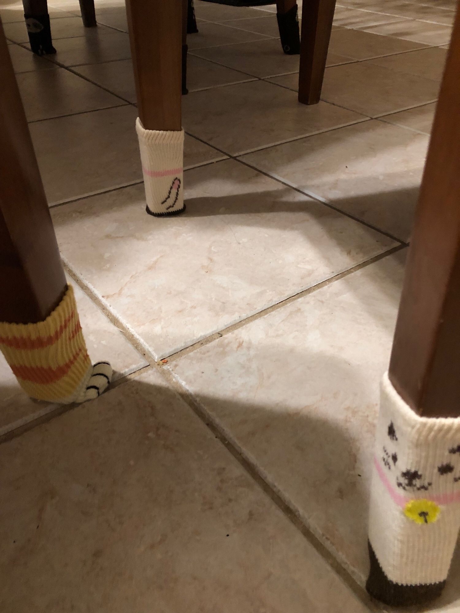 Three chair legs with furniture socks. Nearest sock is a cute white cartoony cat face with a pink collar and bell, left sock is a is like a ginger tabby’s foot with its little white paws protruding at the bottom. The far sock is the back of the first with the pink collar going around above a … um… tail with a pink tip that looks nothing like anything anatomically male that could be construed as NSFW. Nope. Nothing like that.