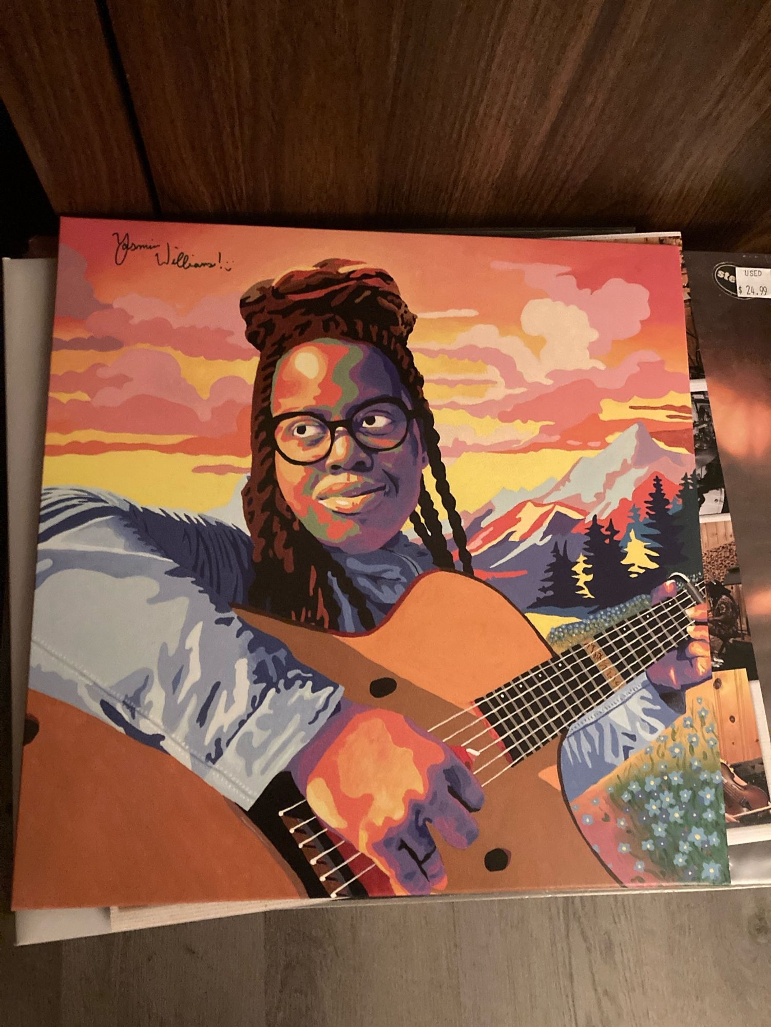 An album cover, the artist in stylized color illustration playing an acoustic guitar with sky and mountains behind them.