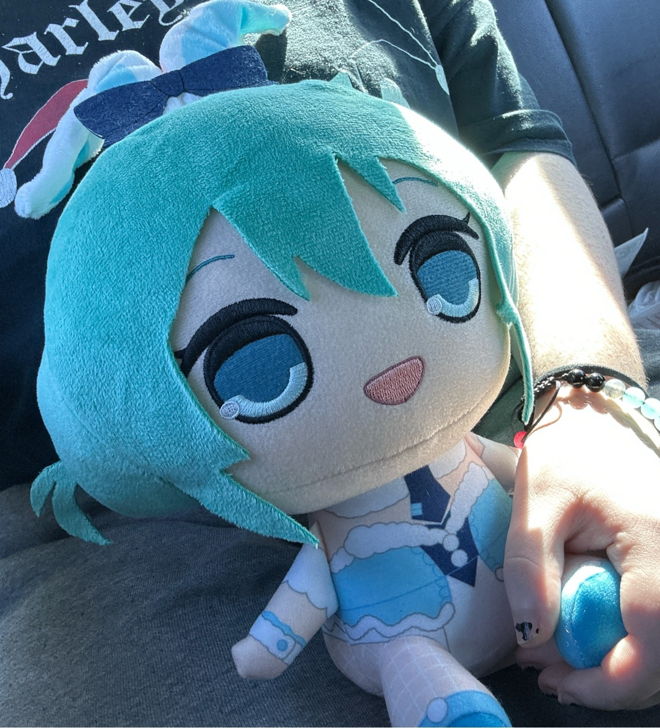 The Hatsune Miku plush from the first image is now being gently held in someone's lap