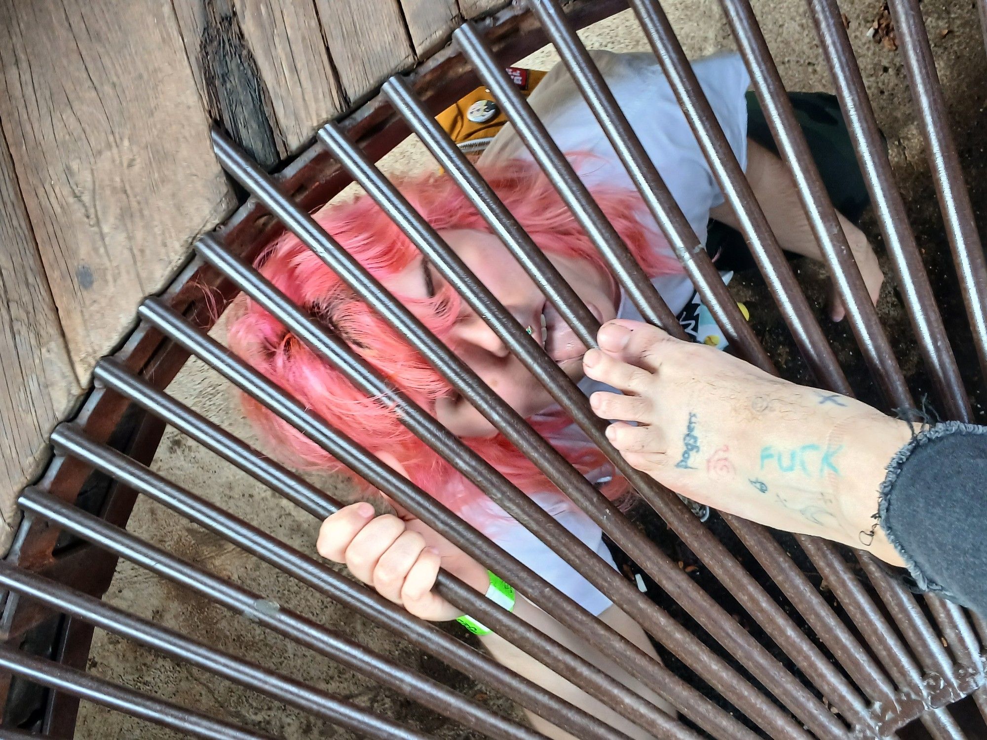 one person under a set of bars with their tongue out, almost licking another persons foot through the bars above them