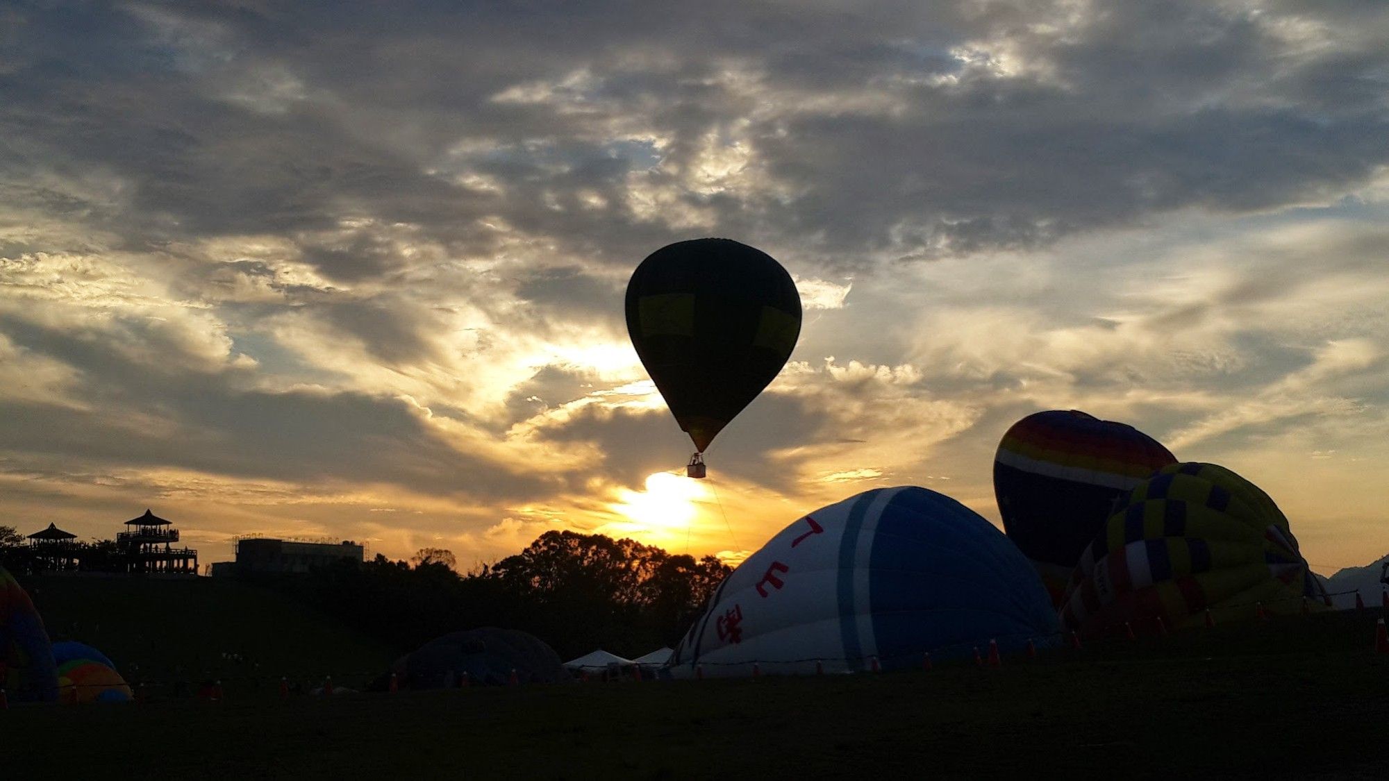 rechts werden 3 Heissluftballons vorbereitet... in der Mitte steigt einer in den Himmel auf... vor dem Sonnenaufgang... links erkennen wir einen Pagodenbau