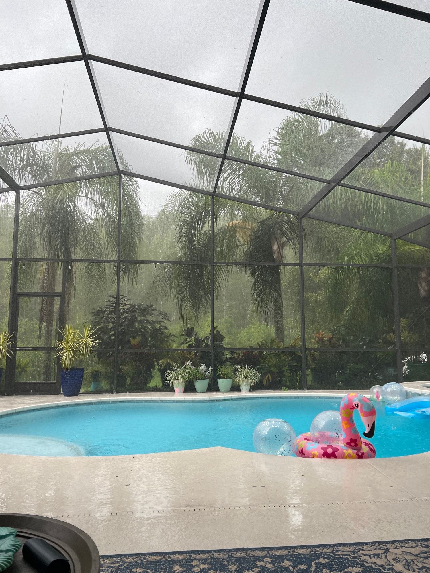 The view of a caged in pool from under the roof. It’s rainy and dark and the sky is gray