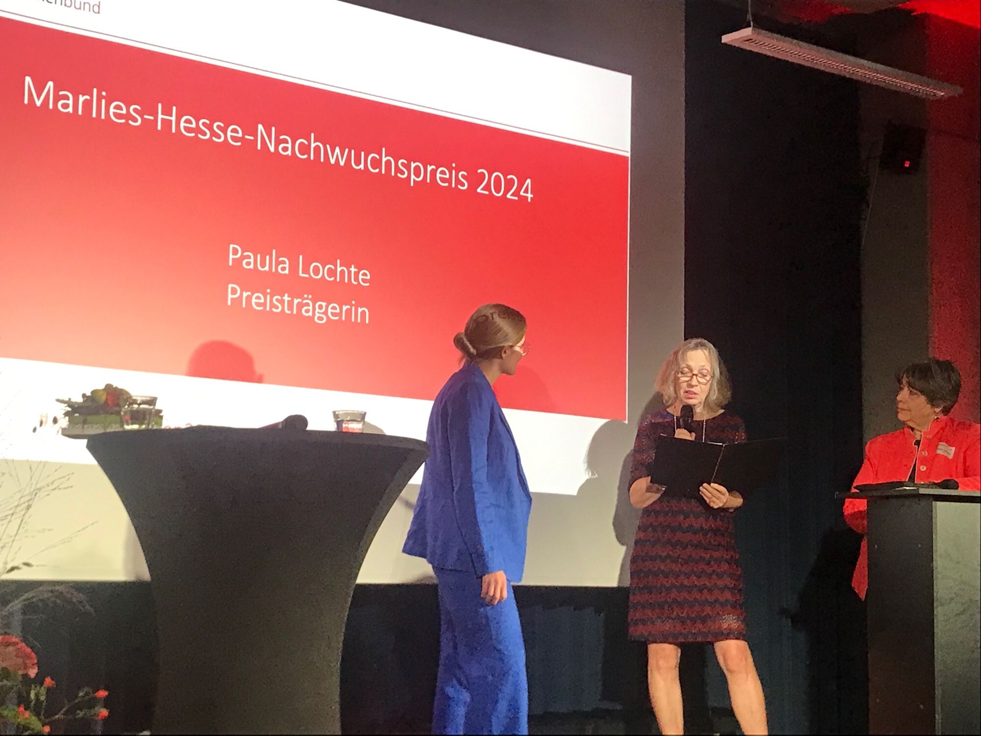 Paula Lochte im Blauen Hosenanzug auf der Bühne mit 2 Frauen auf der Bühne