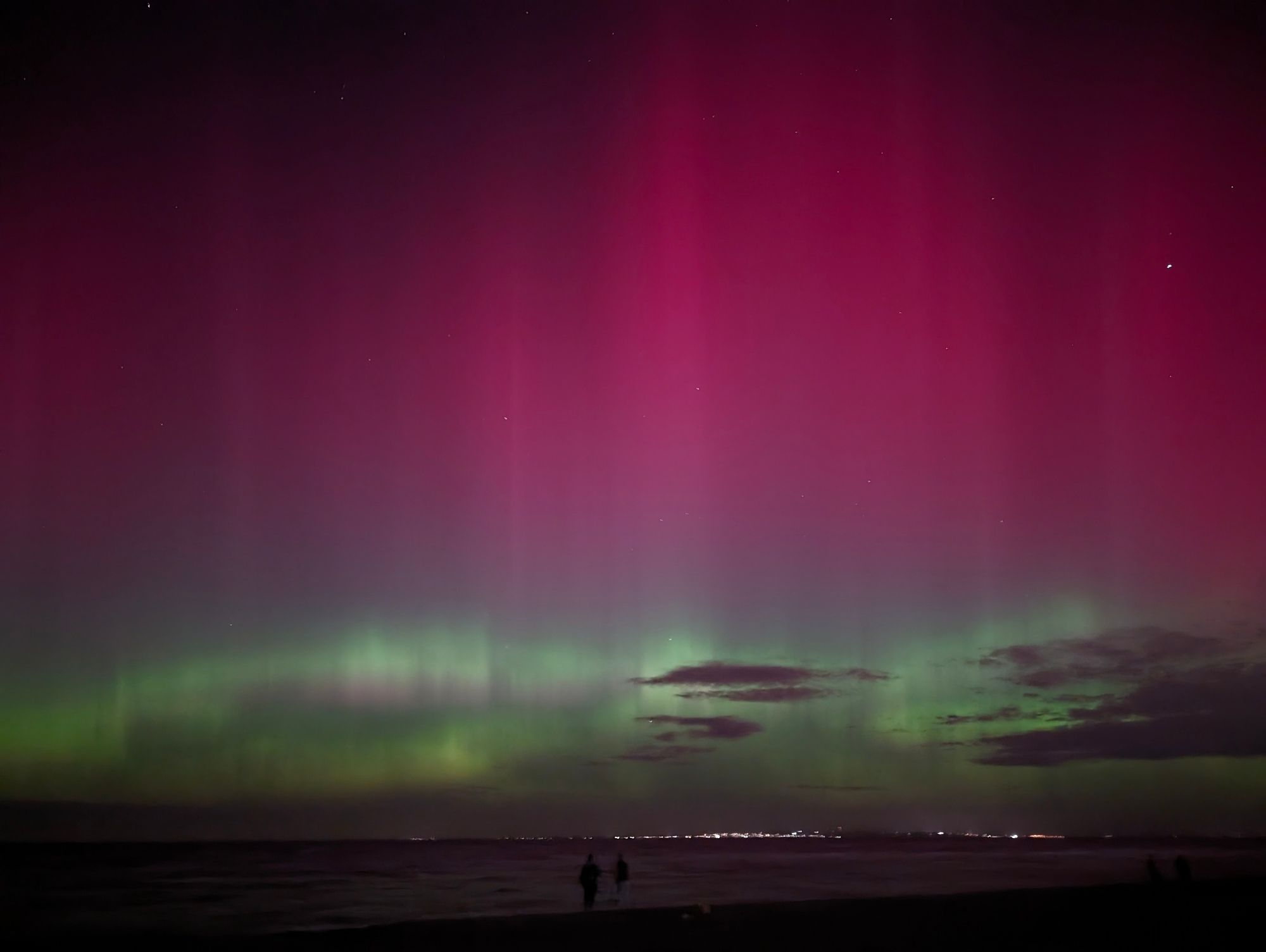 An aurora by the beachside. The aurora contains pink pillars with green shimmers towards its base