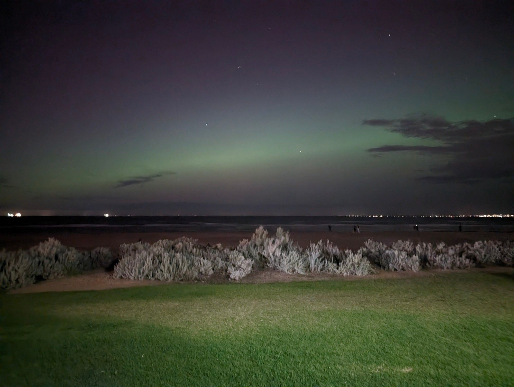 An aurora seen from a beach. The aurora appears as a green glow