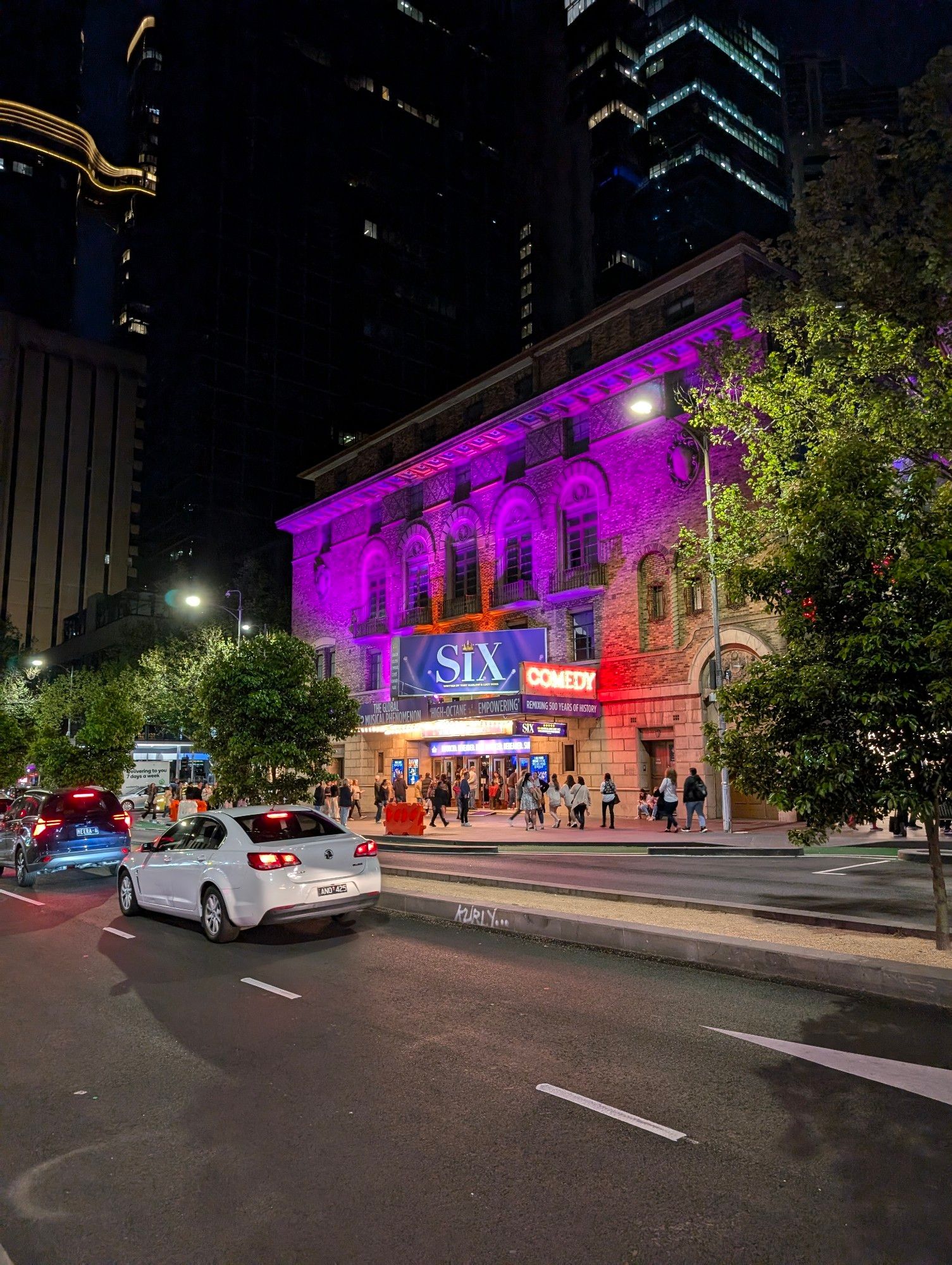 Melbourne's Comedy Theatre lit up in purple. There is a banner promoting Six the Musical