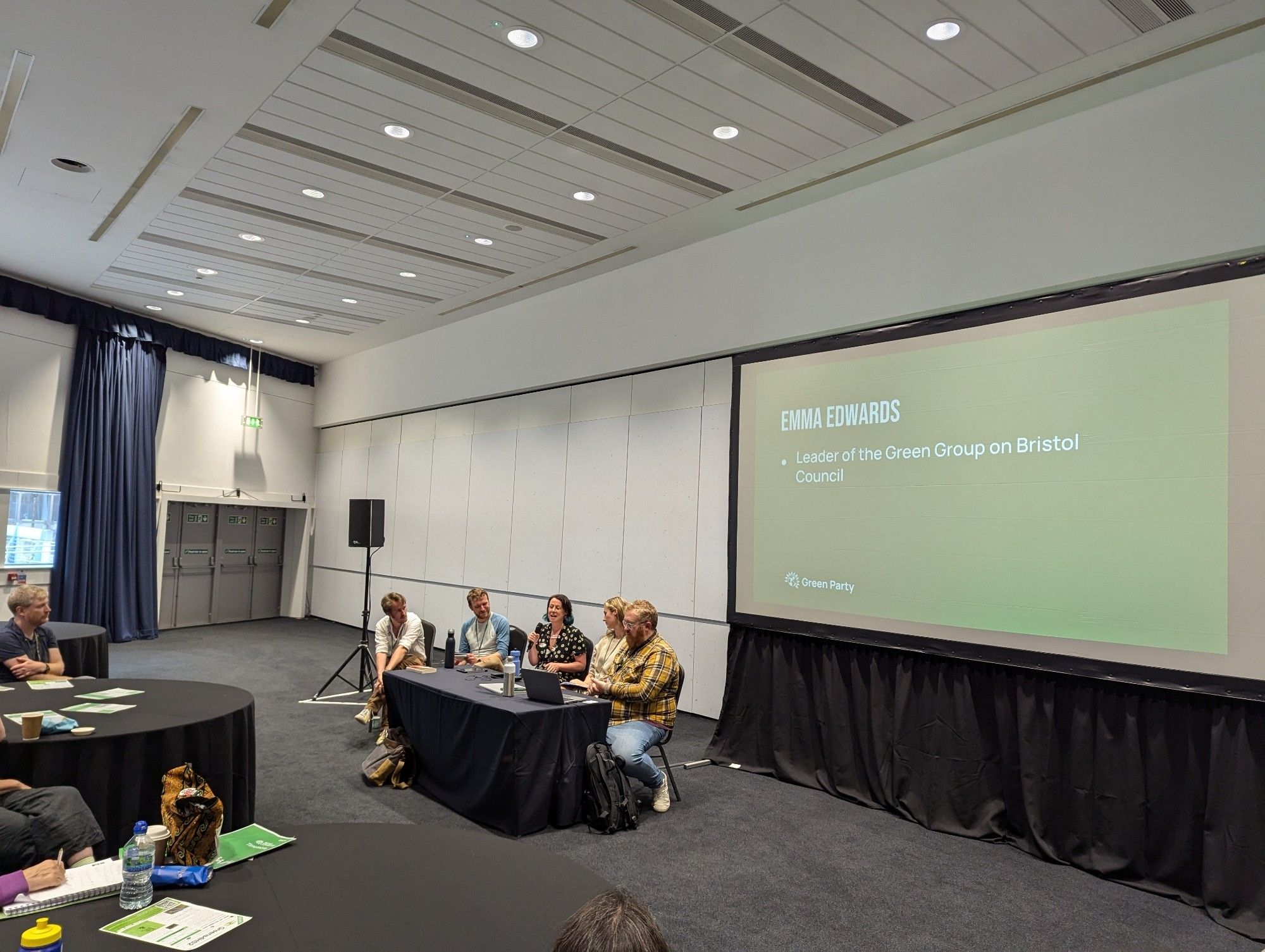 A panel of 4 people plus 1 chair sitting at a table in front of a projector screen