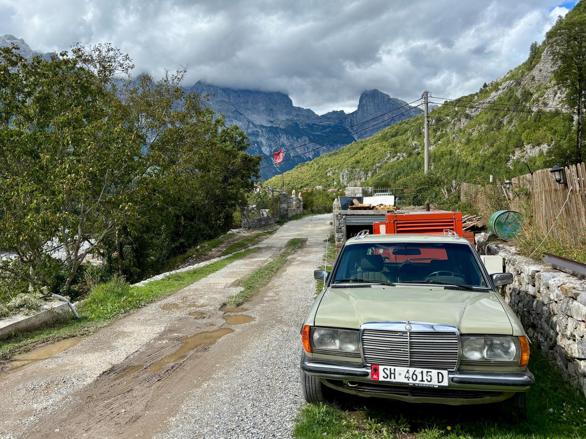 A shabby light green W123-generation Mercedes-Benz estate car parked next to a rough country road in Theth, Albania