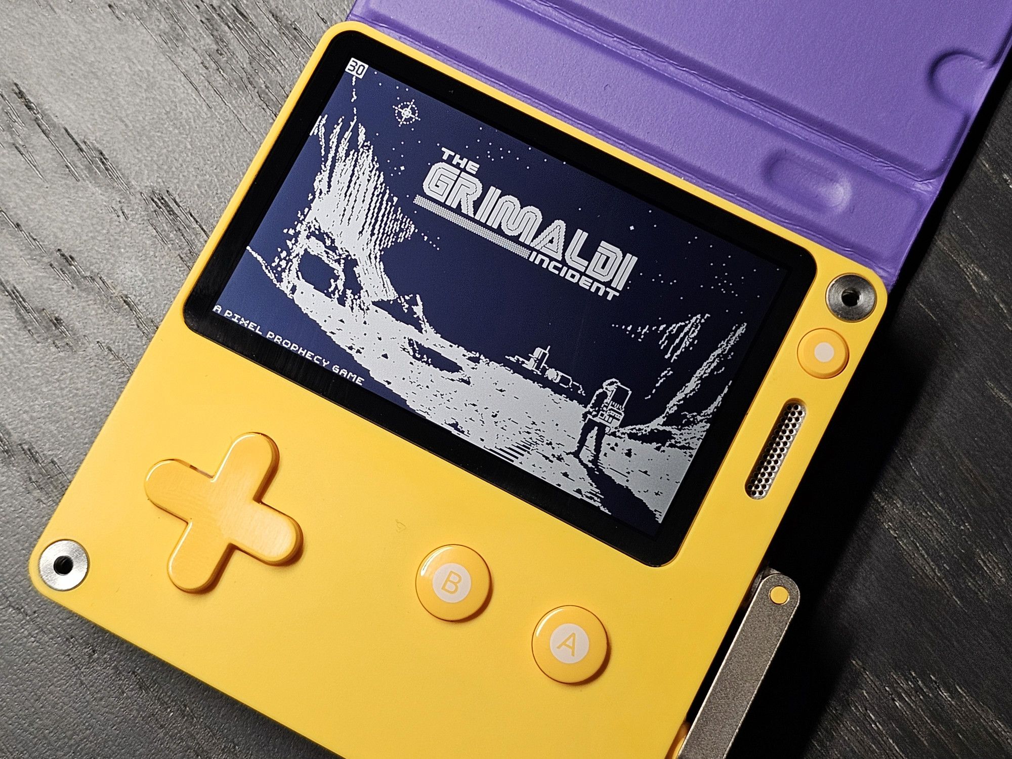 Photo of the play.date handheld showing the title screen of my pet project: It shows an astronaut looking at a moon base in the dark part of a crater. The logo reads "The Grimaldi Incident"