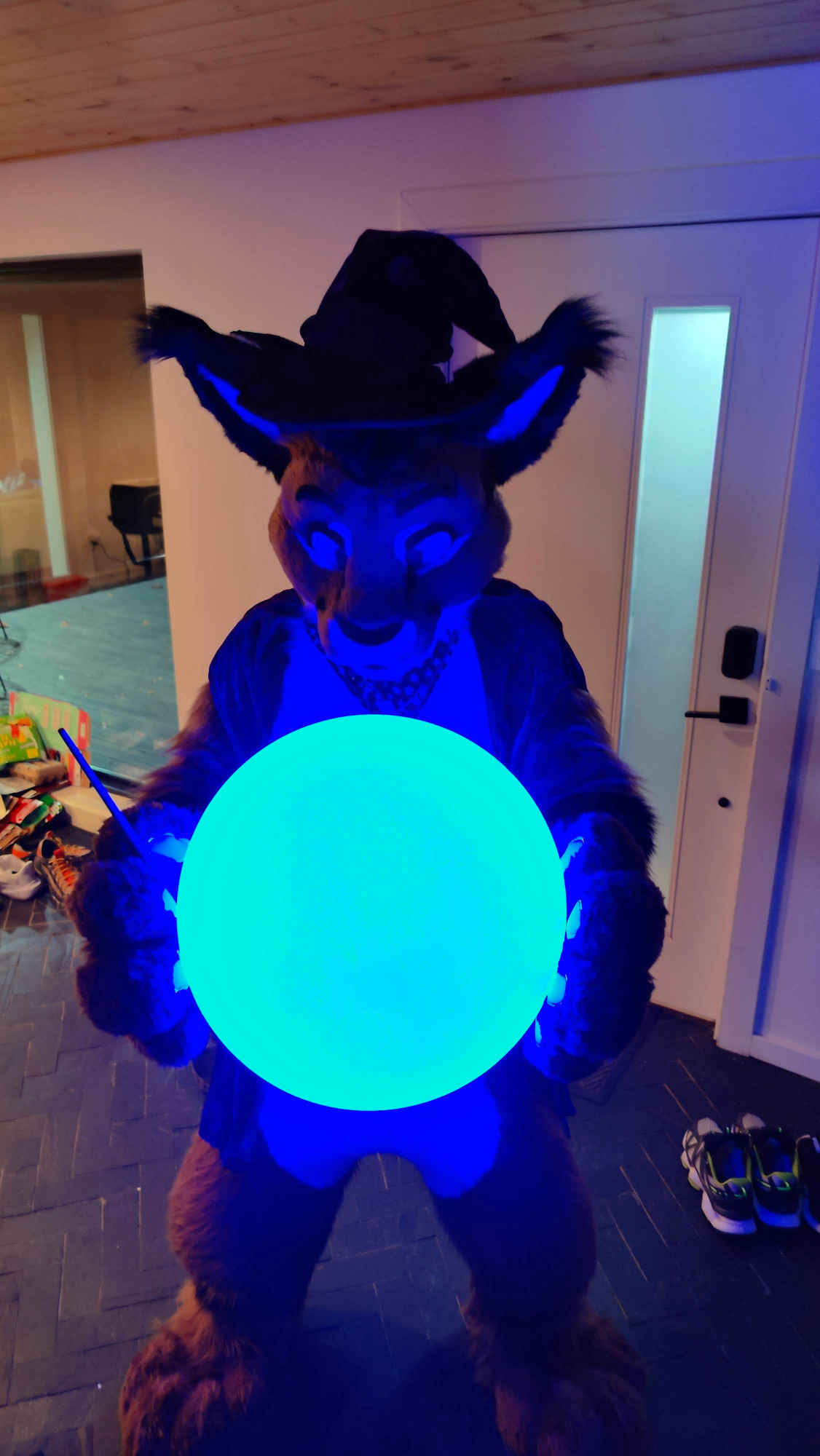 Cooper the Slightly Wise, a caracal fursuiter in a wizard costume, looking down at a large, glowing blue orb between his handpaws.