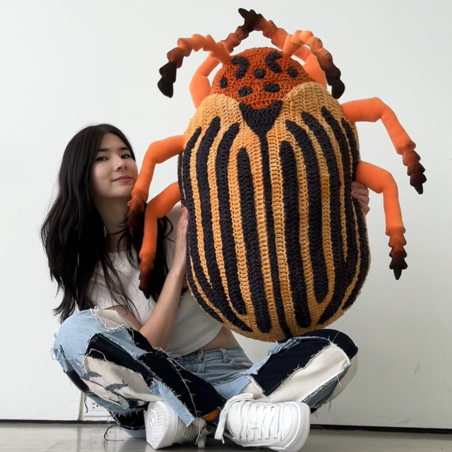 girl holding up giant crochet colorado potato beetle