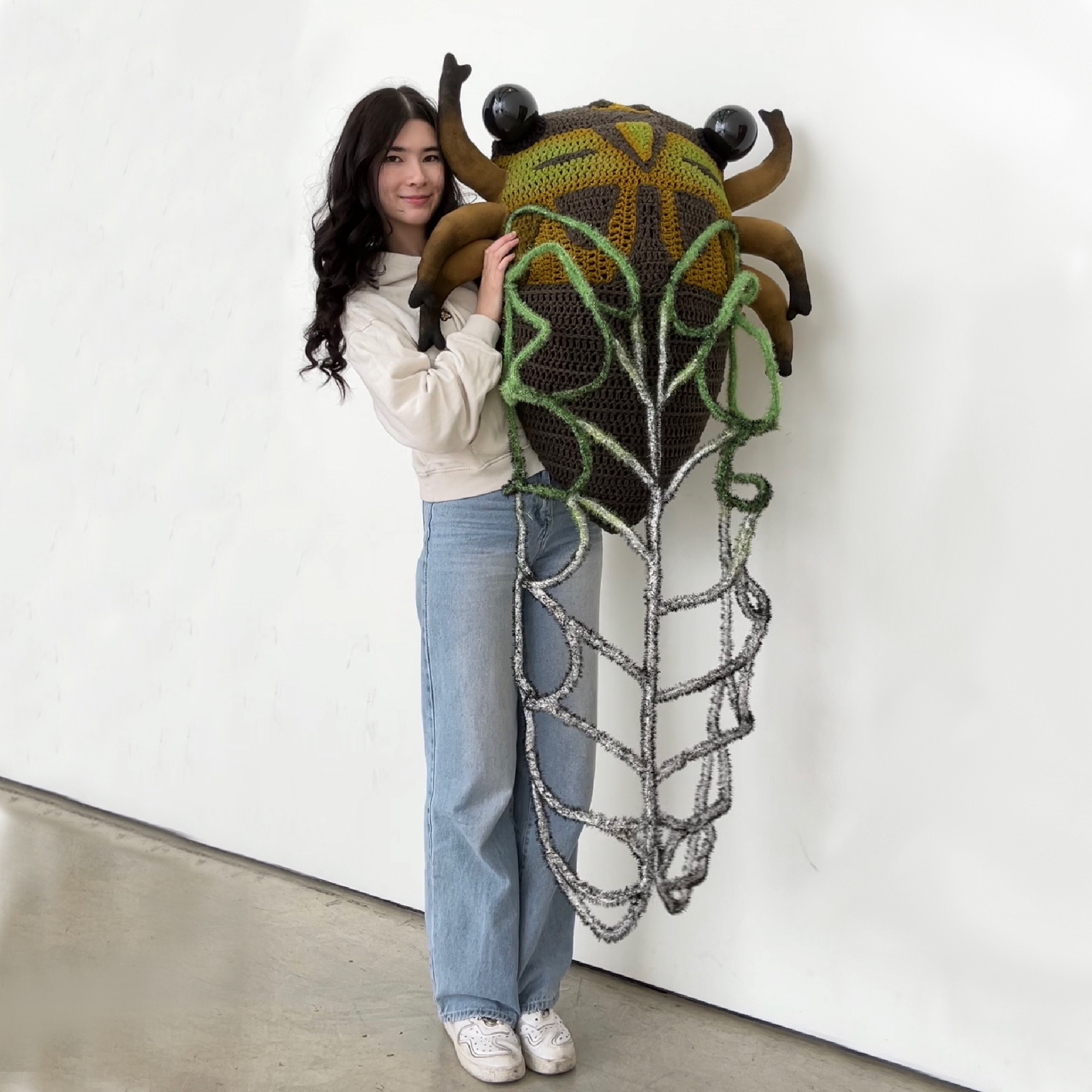 girl holding up giant cicada sculpture