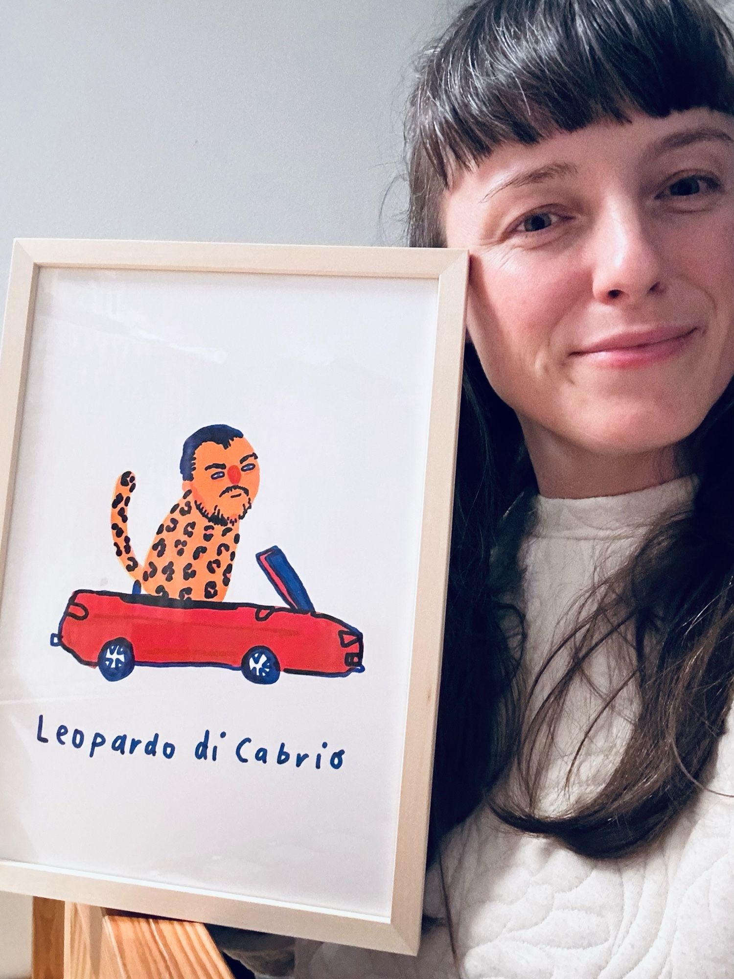 Selfie von Ulschka. Sie zeigt ein Bild im Bilderrahmen in die Kamera. Darauf ist eine Illustration: ein rotes Cabrio, drin sieht ein Leopard mit dem Gesicht von Leonardo Di Caprio. Darunter steht „Leopardo du Cabrio“.