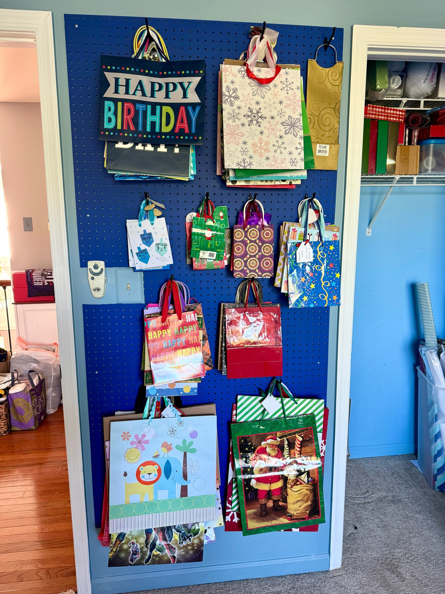 Many assorted gift bags, hung in size order on a pegboard wall in a triumph of adulthood