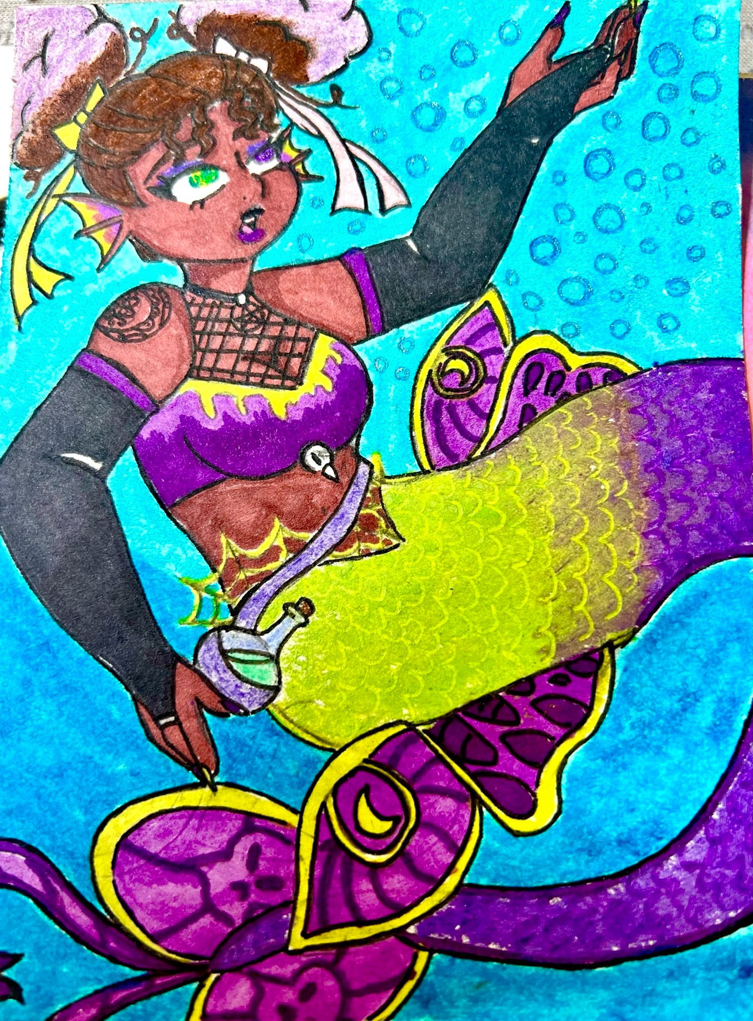 The image portrays a vibrant and colorful illustration of a mermaid. The mermaid has deep brown skin and curly hair styled in two puffs, each adorned with yellow ribbons and white cloth. Her wide eyes are strikingly multicolored, with purple and green hues. She has fish-like fins protruding from her cheeks. A patterned tattoo decorates her right shoulder. Her ensemble includes a purple top with a netted overlay and yellow details, and elbow-length black gloves with purple cuffs. The mermaid's tail is vivid, transitioning from lime green with scale patterns to a deep purple, adorned with intricate magenta and yellow designs. She is holding a small round bottle in her left hand. The background is a bright blue with bubbles scattered throughout, simulating an underwater scene.