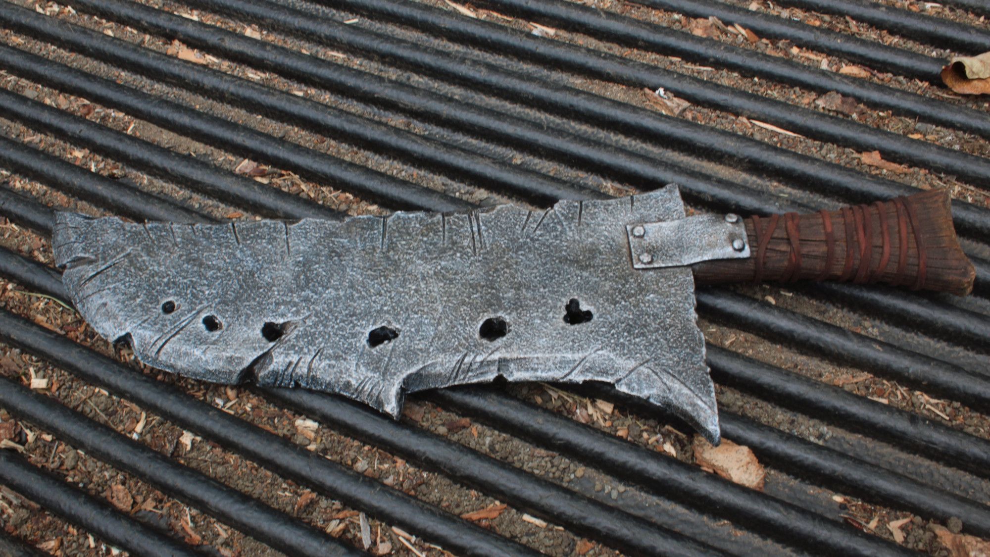 A jagged looking wide blade, with dings and dents and a pitted appearance, along with a handle that's just a branch