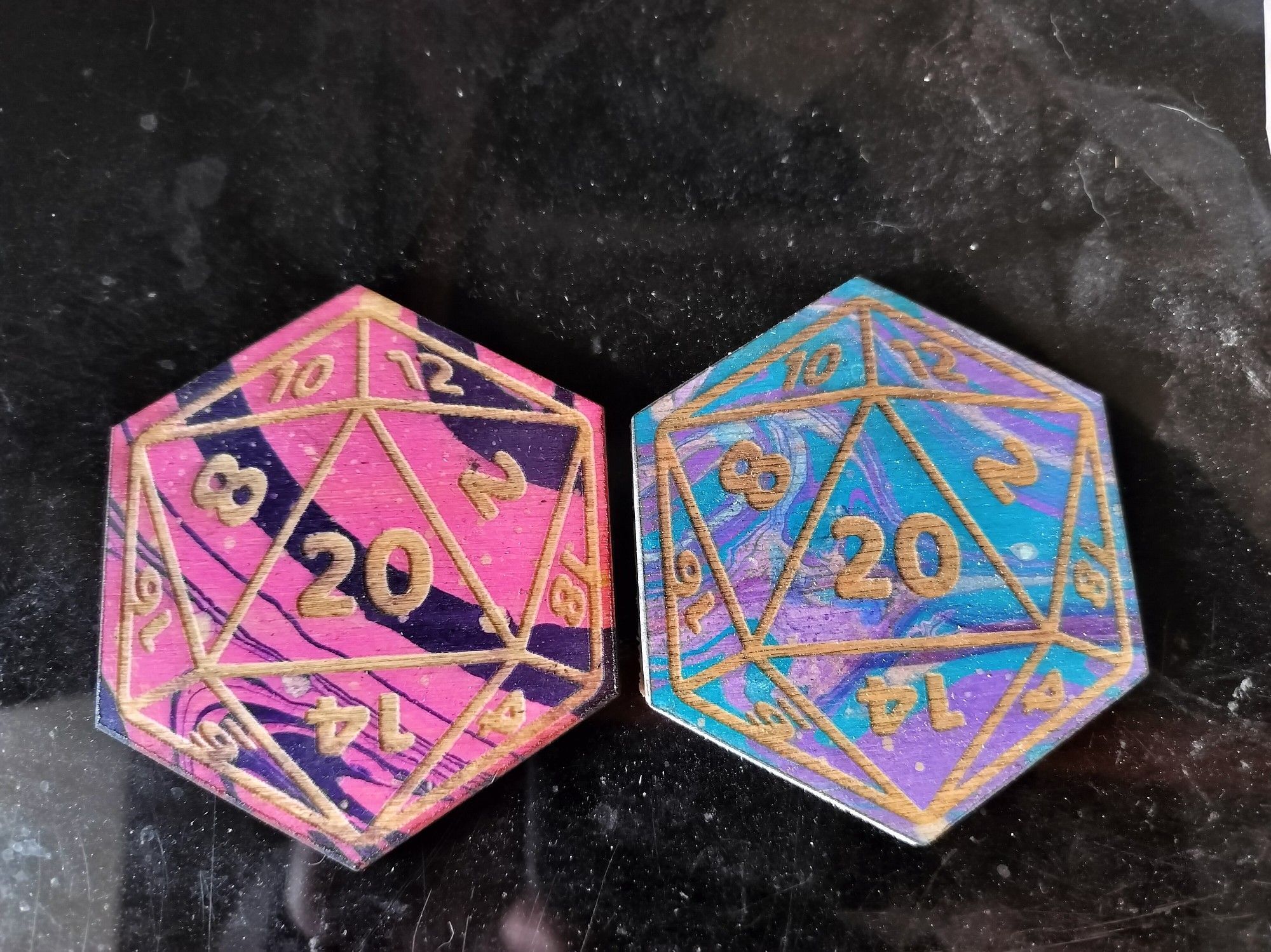 Two d20 shaped coasters painted in swirly marble patterns