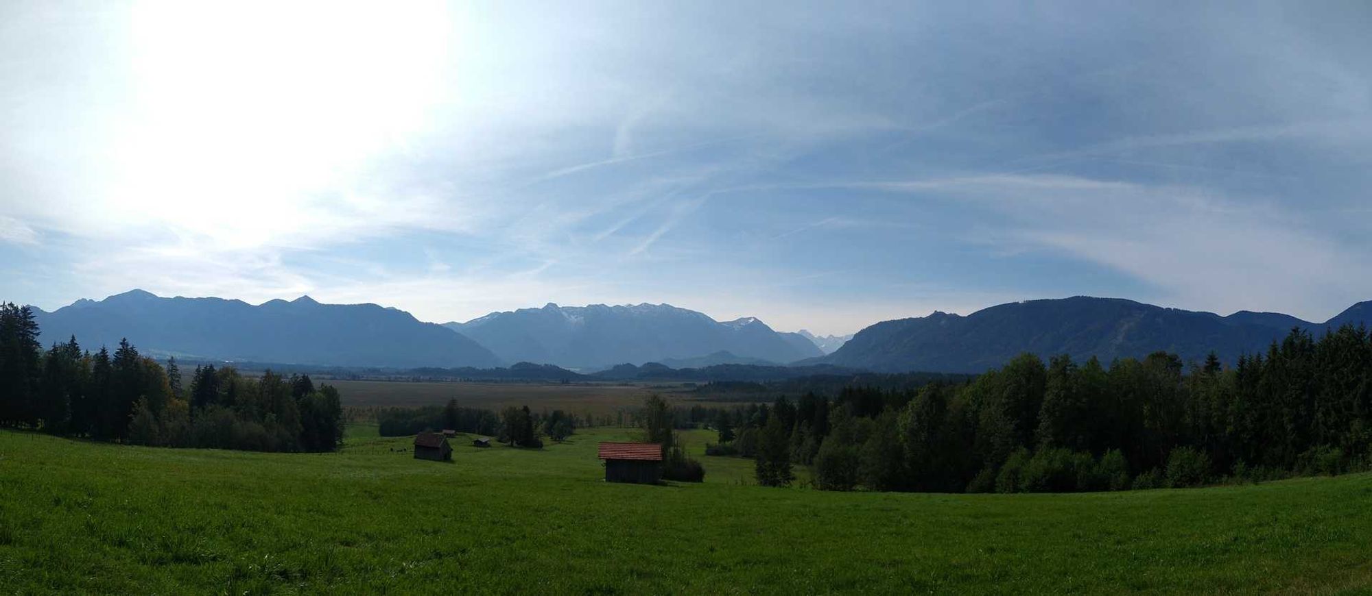 Panoramablick über das Murnauer Moos: vorne Wiesen, teilweise mit Bewuchs, am Horizont Estergebirge, Zugspitze und Ammergauer Alpen.