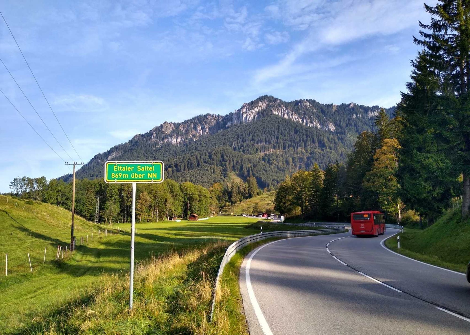 Blick vom Ettaler Sattel Richtung Ammergauer Alpen: vorne ein Schild, 869m über NN, rechts die Straße, dahinter Berge.