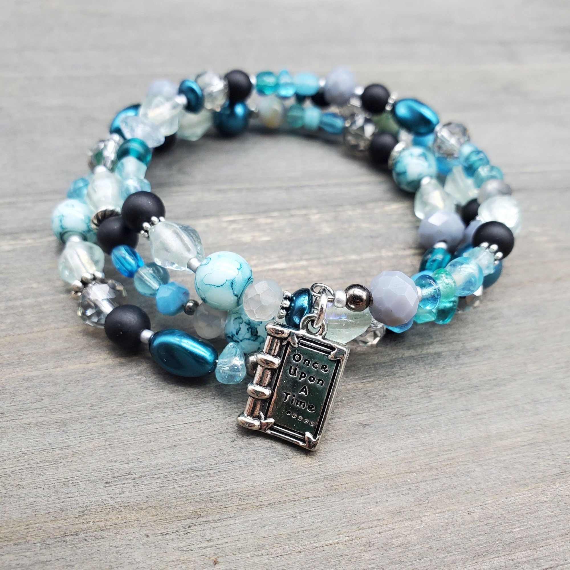 a coil memory wire bracelet in teal and black finished with a once upon a time book charm