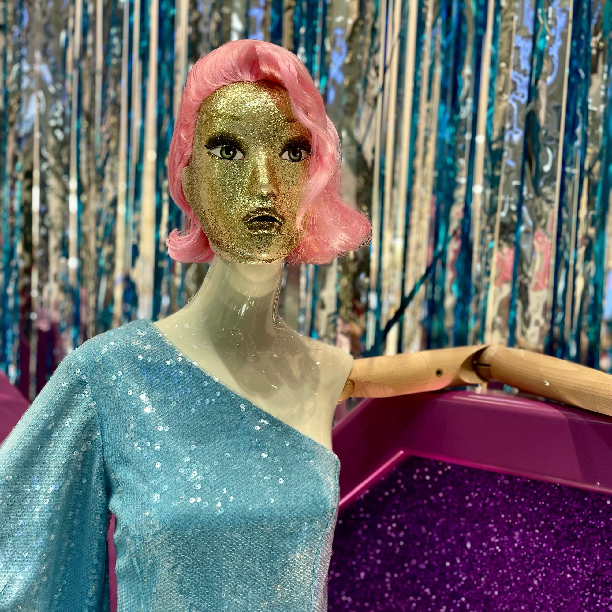 Mannequin with off the shoulder sparkly blue dress and bobbed pink hair.