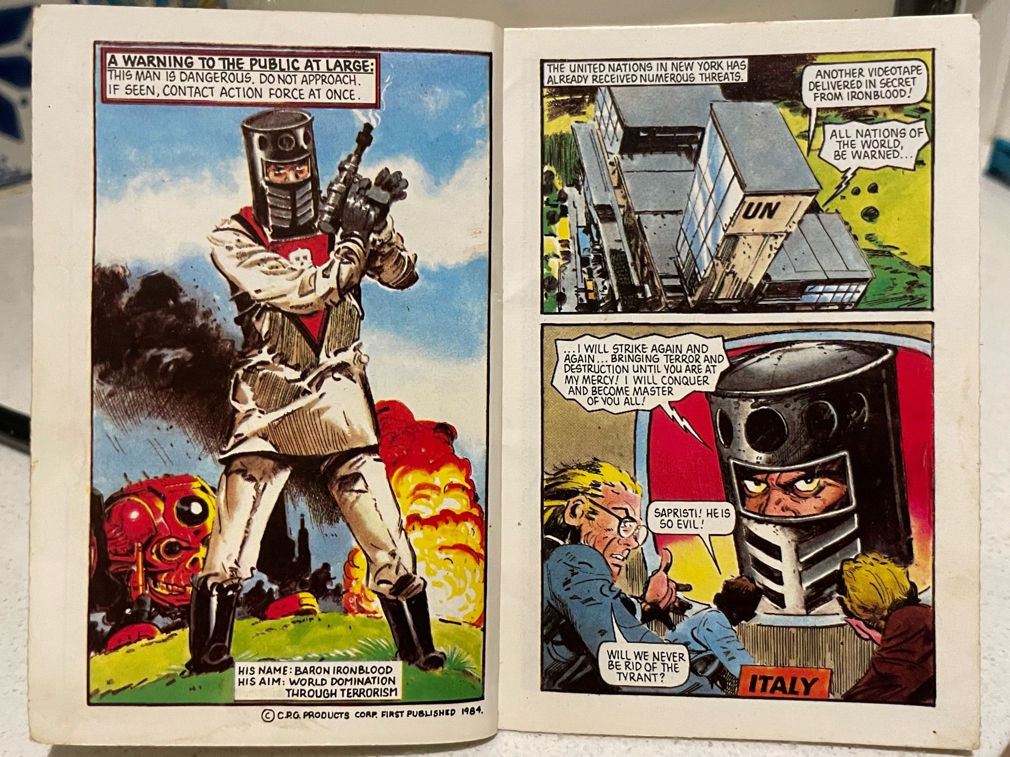 A comic-style illustration featuring a villain named Baron Ironblood, depicted in a threatening pose with a gun. The background shows explosions and a building labeled "UN." Text warns of danger and expresses his intent for world domination through terrorism. Other characters appear alarmed at his broadcast.