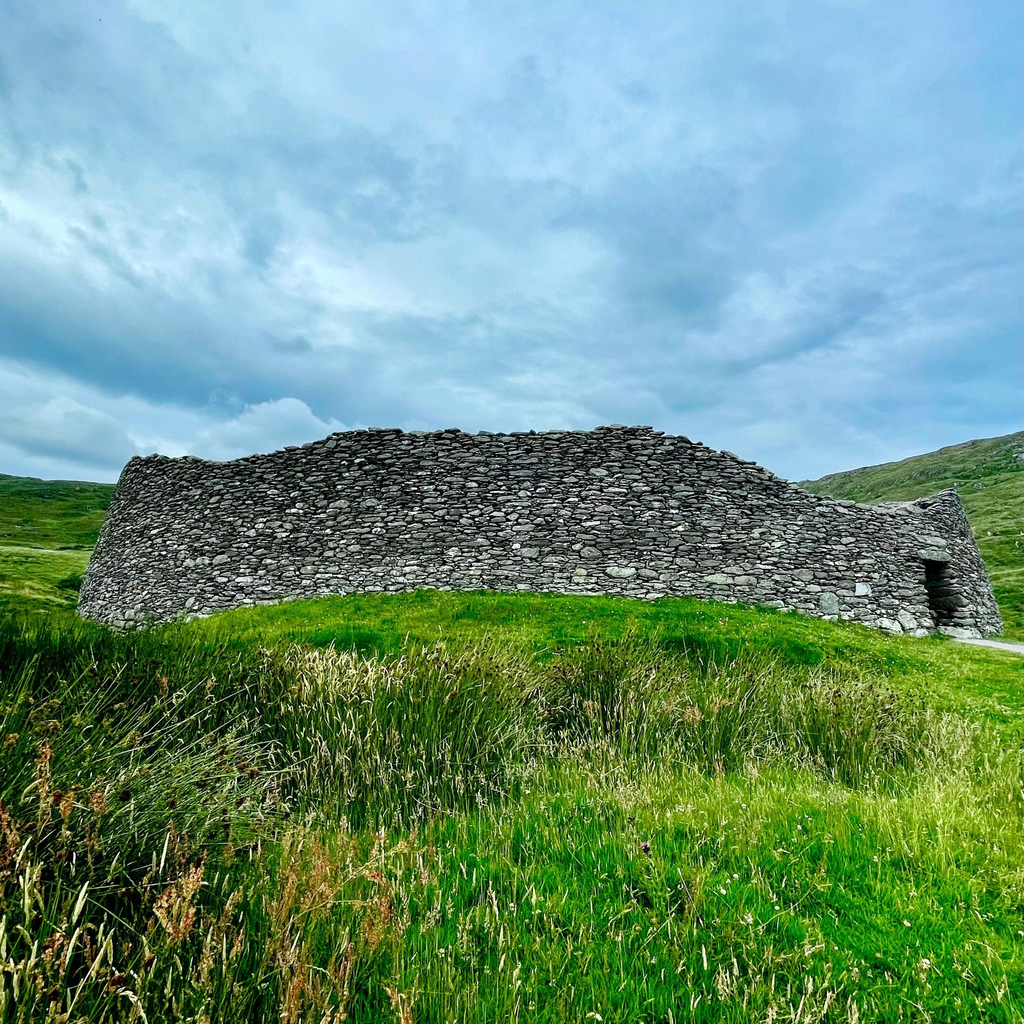 Ancient stone structure in a grassy field under a cloudy sky