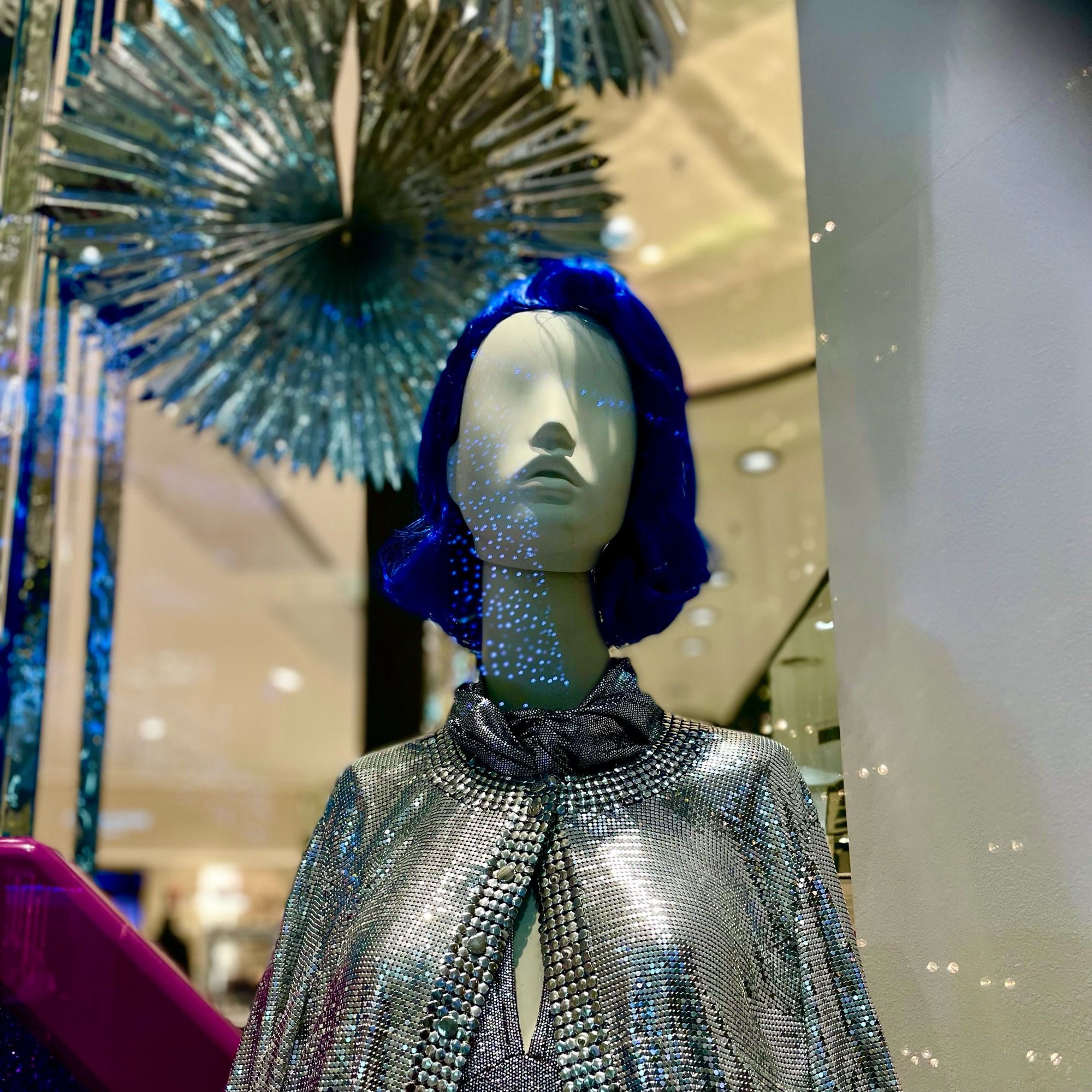 Blue haired eyeless mannequin in silver clothes.