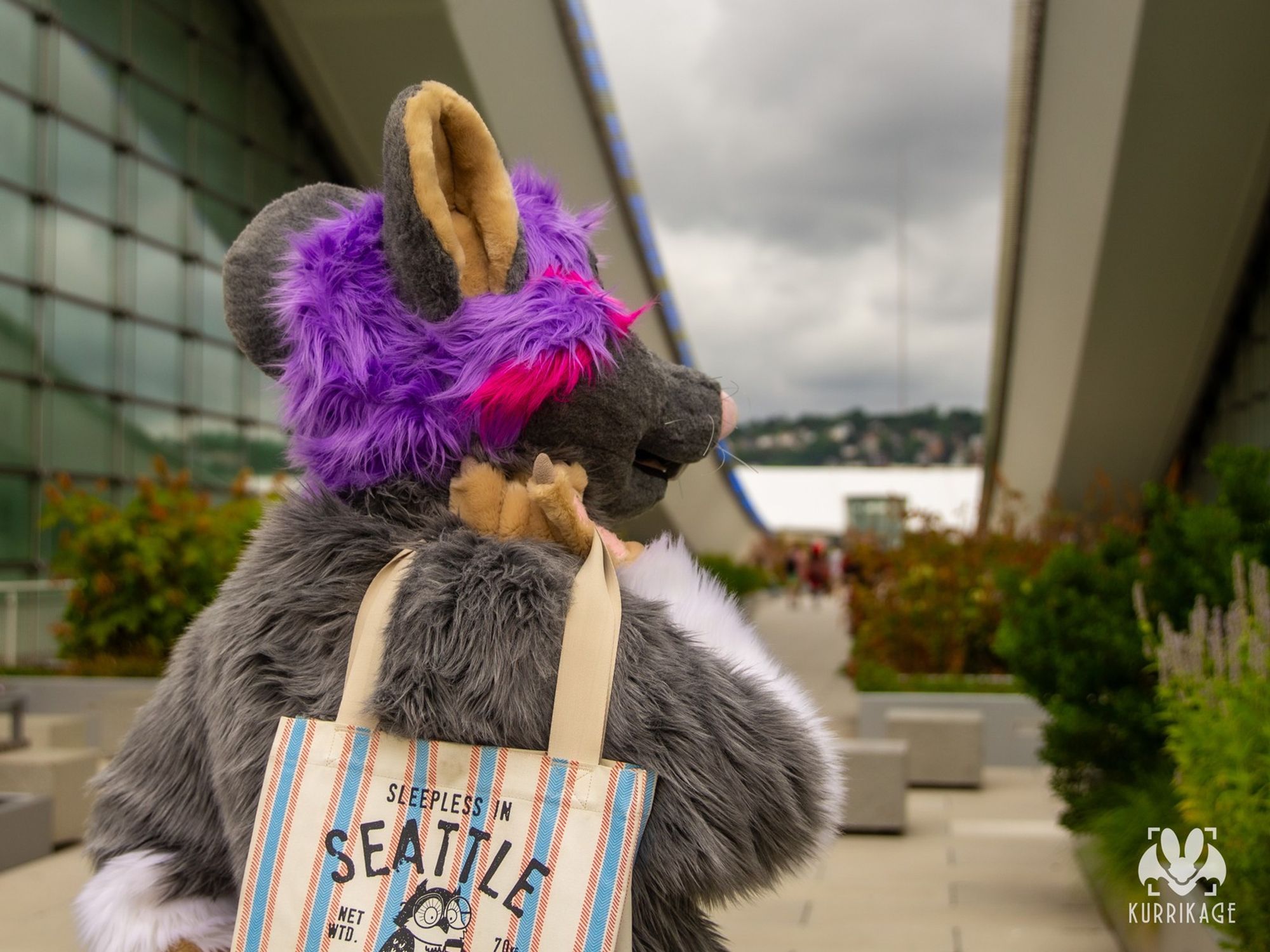 A rat fursuit holding a bag over their shoulder viewed from behind.