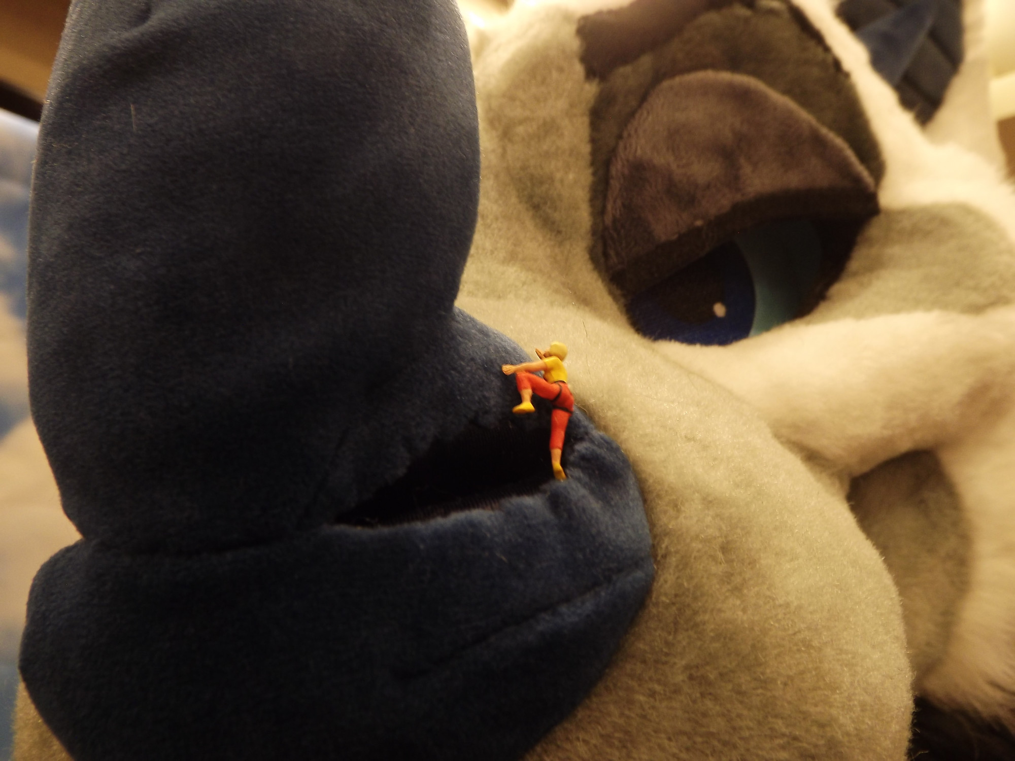 A close up of a bat fursuit nose with a tiny climbing person figure scaling up his nose. 