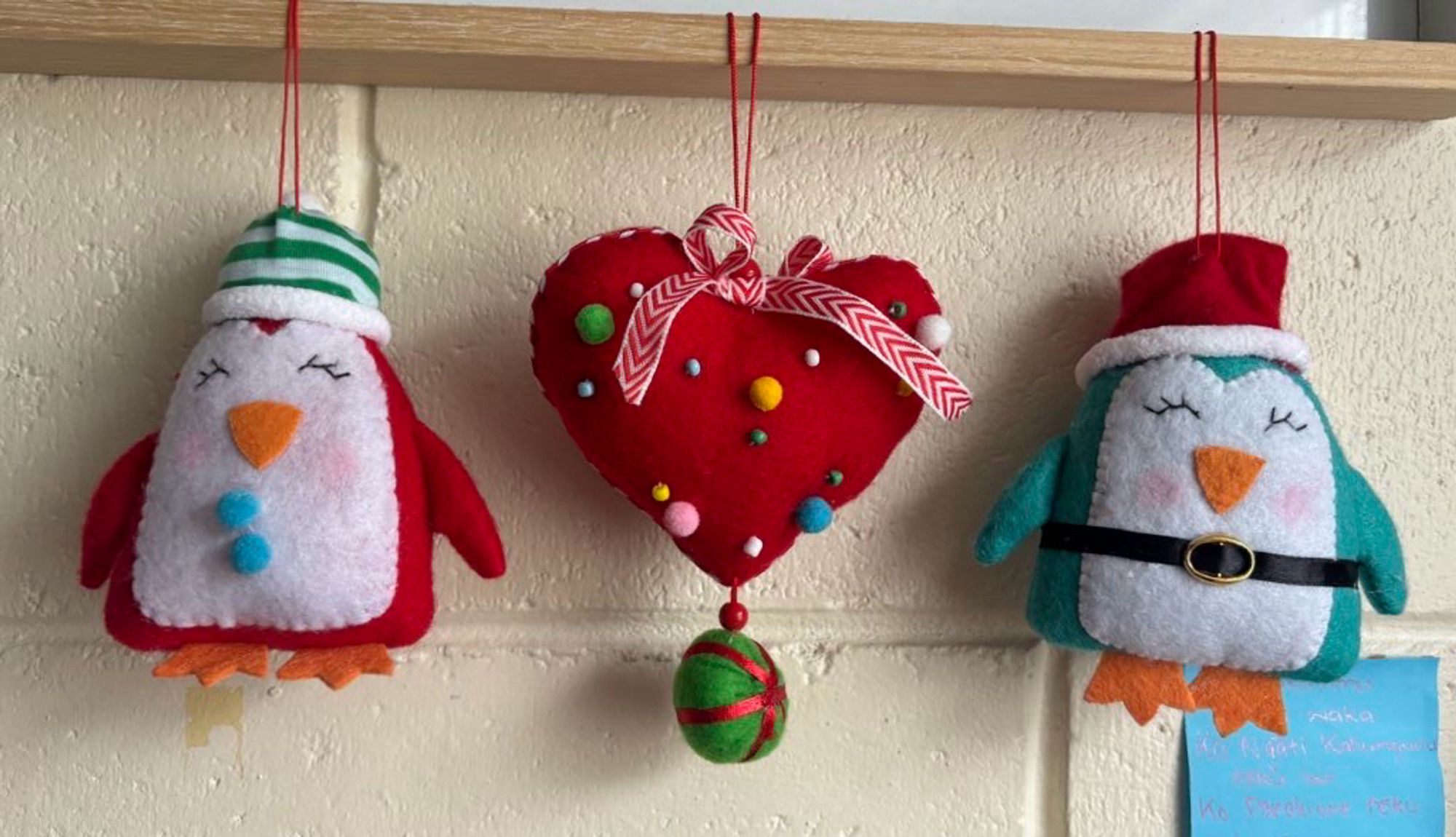 Two felt penguins decorations, one red one blue, hanging either side of a felt heart