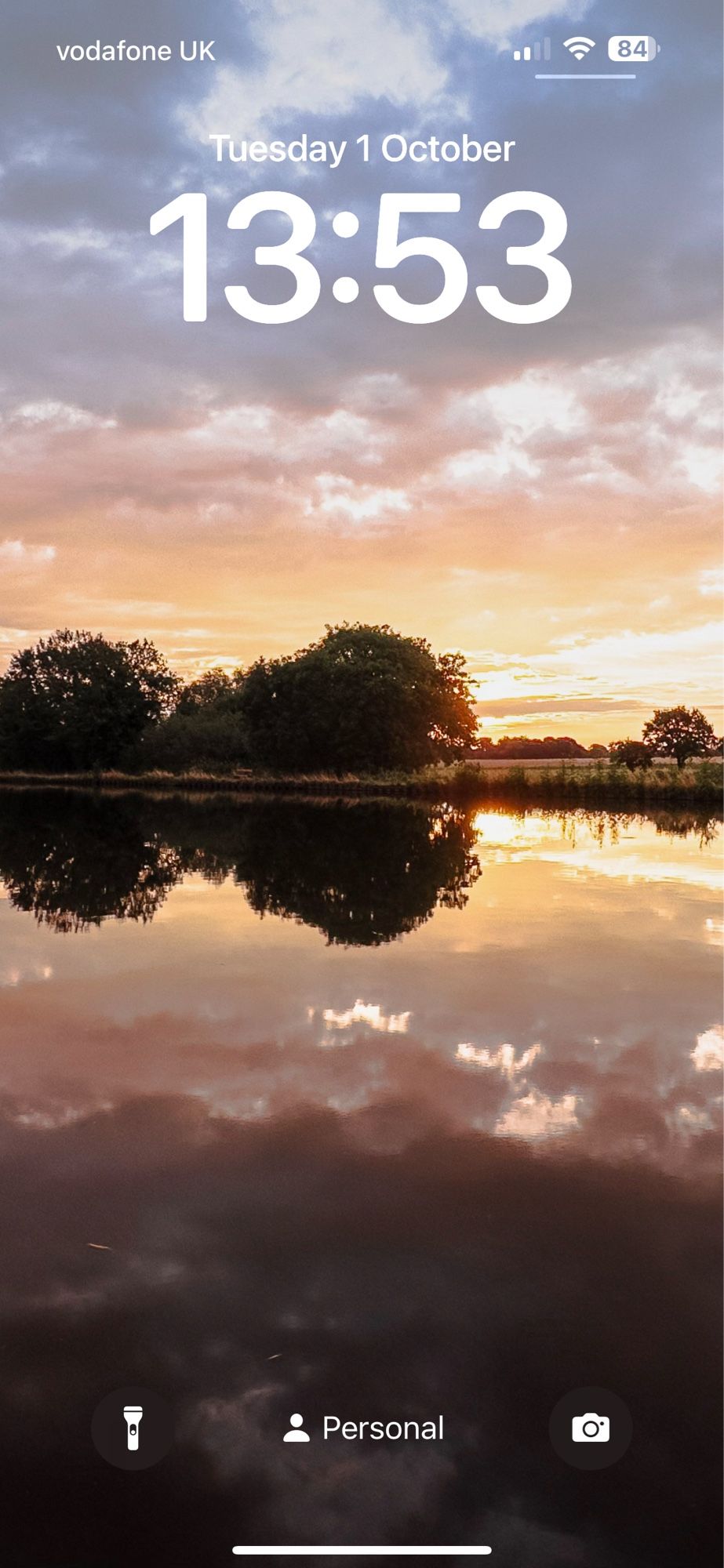 Sunrise over a still canal, trees and sky reflecting in the water