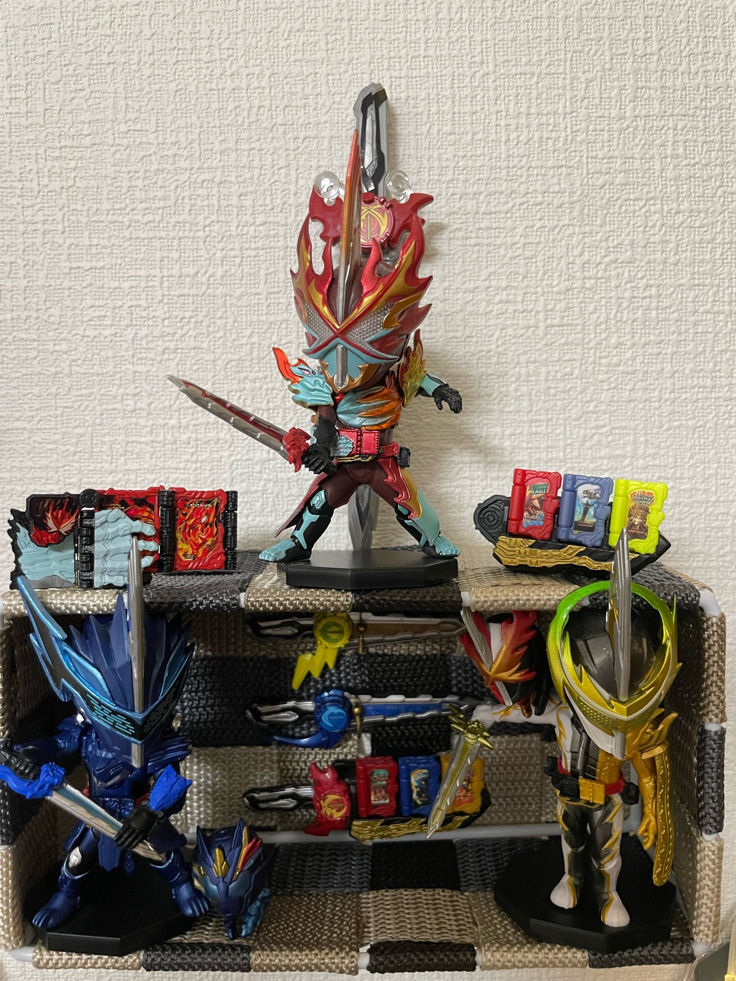 a miniature kamen rider saber display featuring figures of blades, espada, and my favorite suit ever elemental primitive dragon. there are also tiny little versions of their swords pinned behind them, and tiny versions of the belt and the elemental primitive dragon book