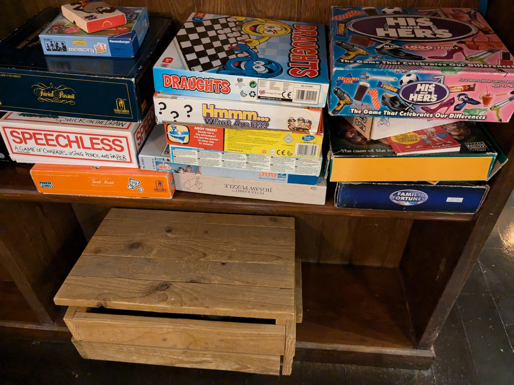 A selection of boxed board games, some traditional and others new, in a wooden cabinet.