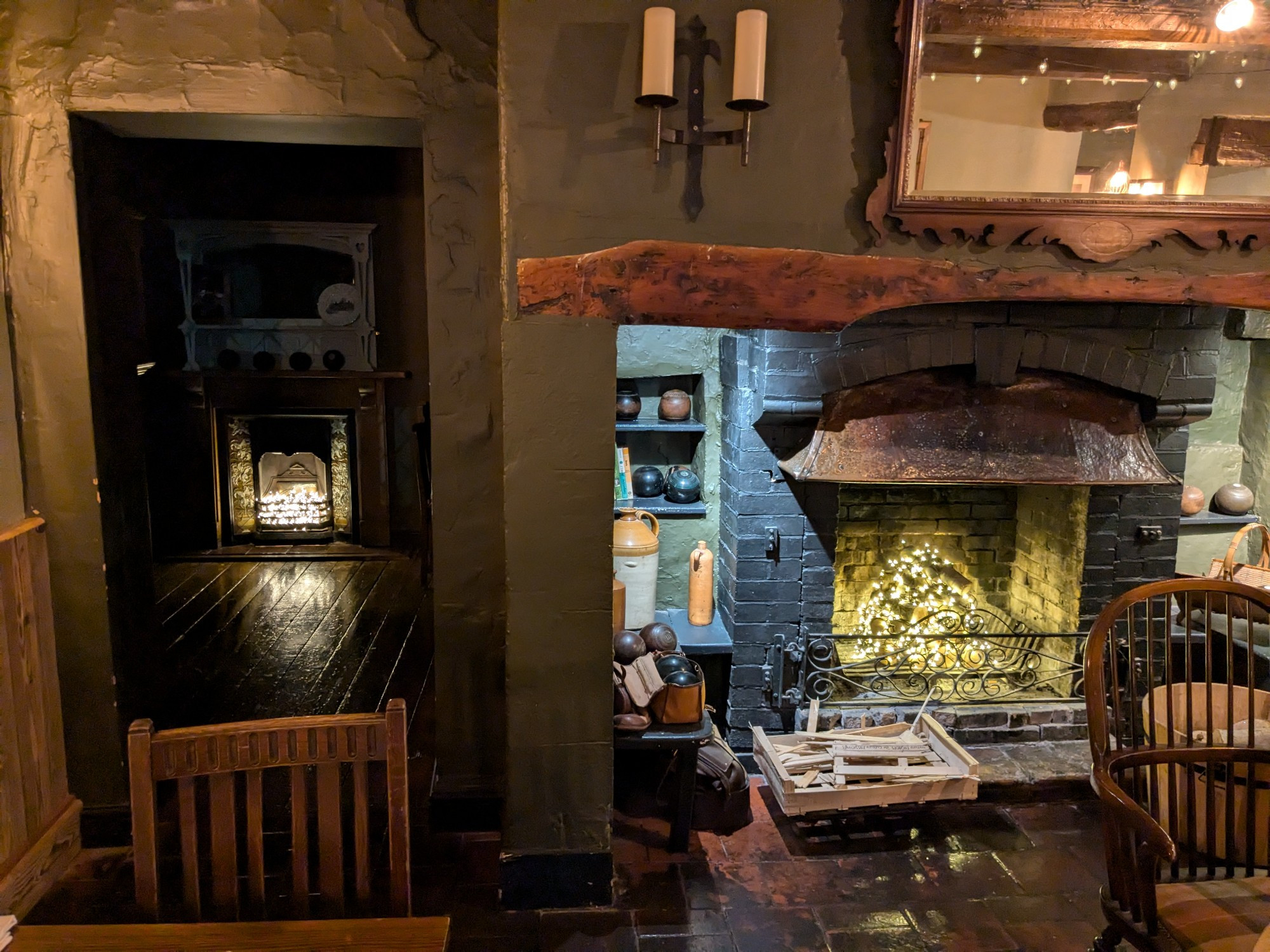 A pub dining room, with a doorway leading to another room (with the lights off). In this and the other room, some subtle electric lights have been arranged in the fireplaces.