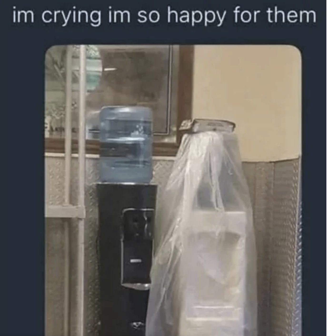 A black water cooler, and a white water cooler with a plastic cover over it like a wedding veil. Text: I’m crying I’m so happy for them.